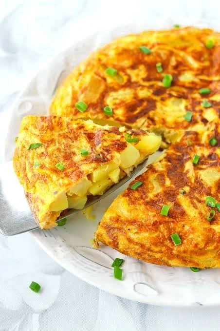 Three pieces of a golden-brown potato omelette garnished with chopped green onions on a white plate.