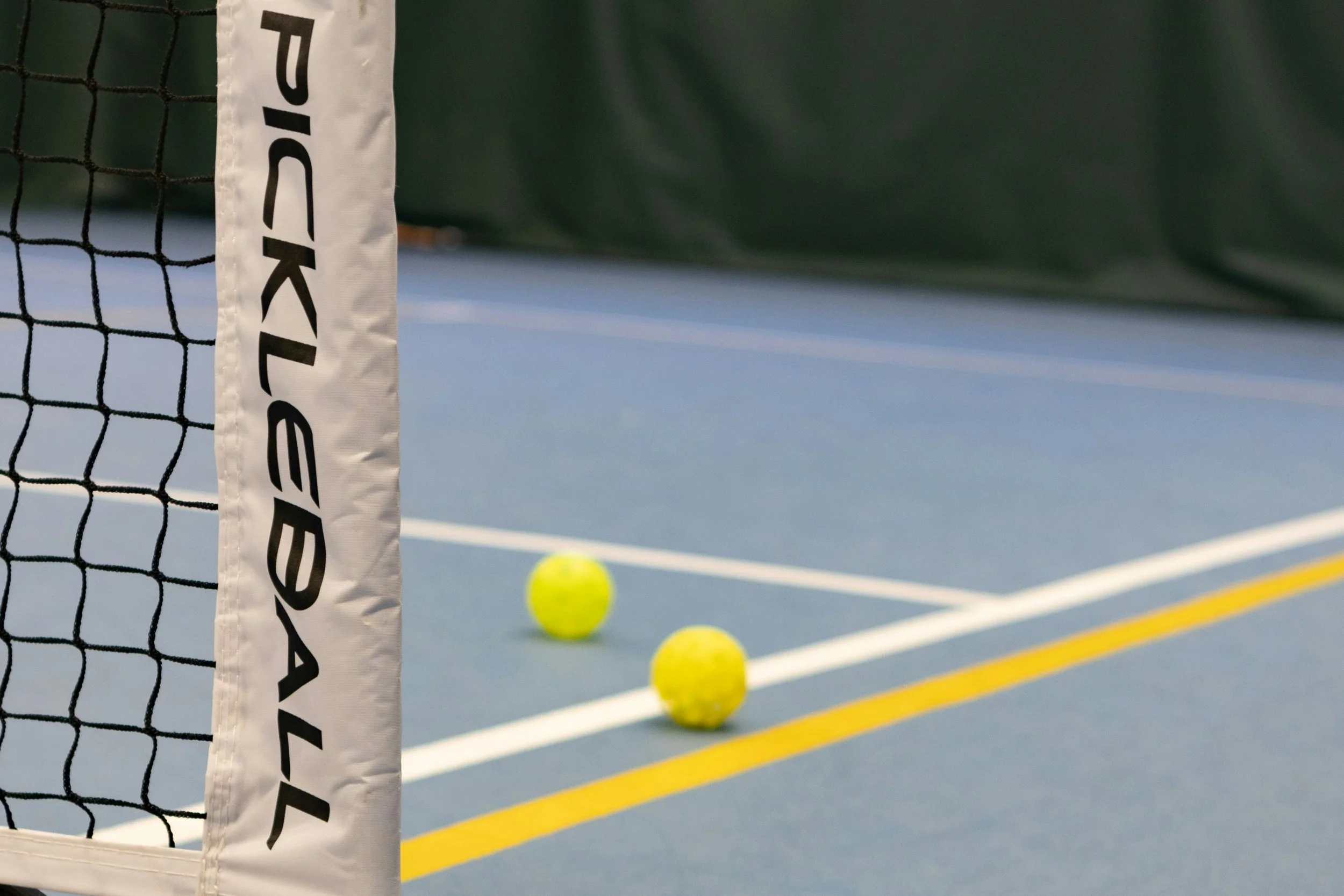 Zoomed in picture of a Pickleball net, court, and two balls resting on the court.
