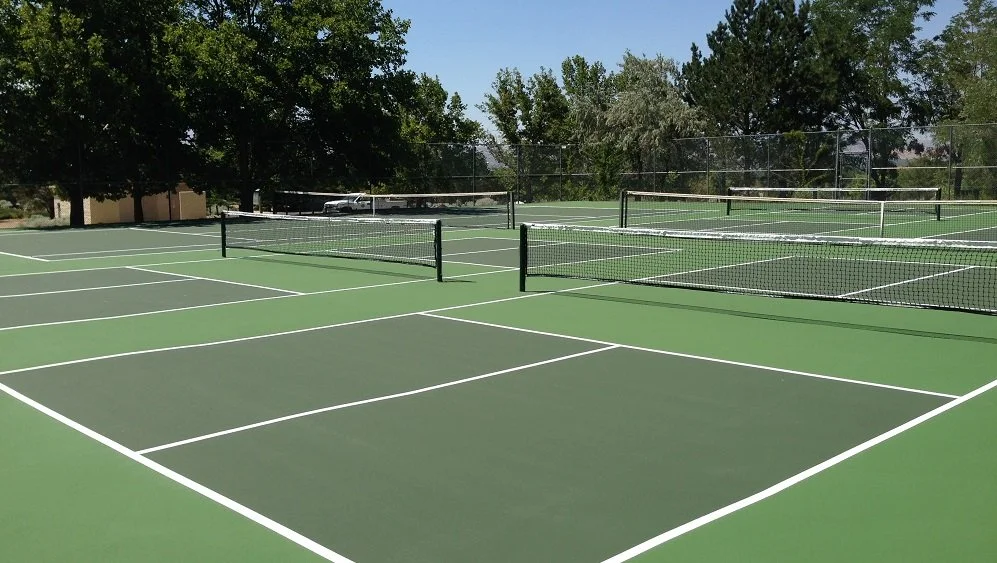Hidden Valley outdoor pickleball court surrounded by a chain-link fence, with mountains in the background and trees casting shadows on the court.