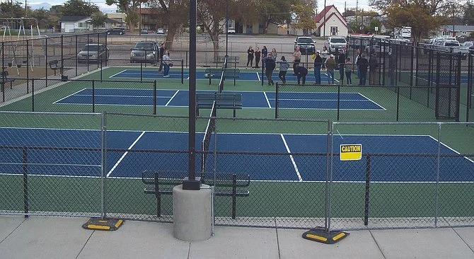 A group of people playing pickleball at Oats Park and watching pickleball on multiple courts inside a fenced area.