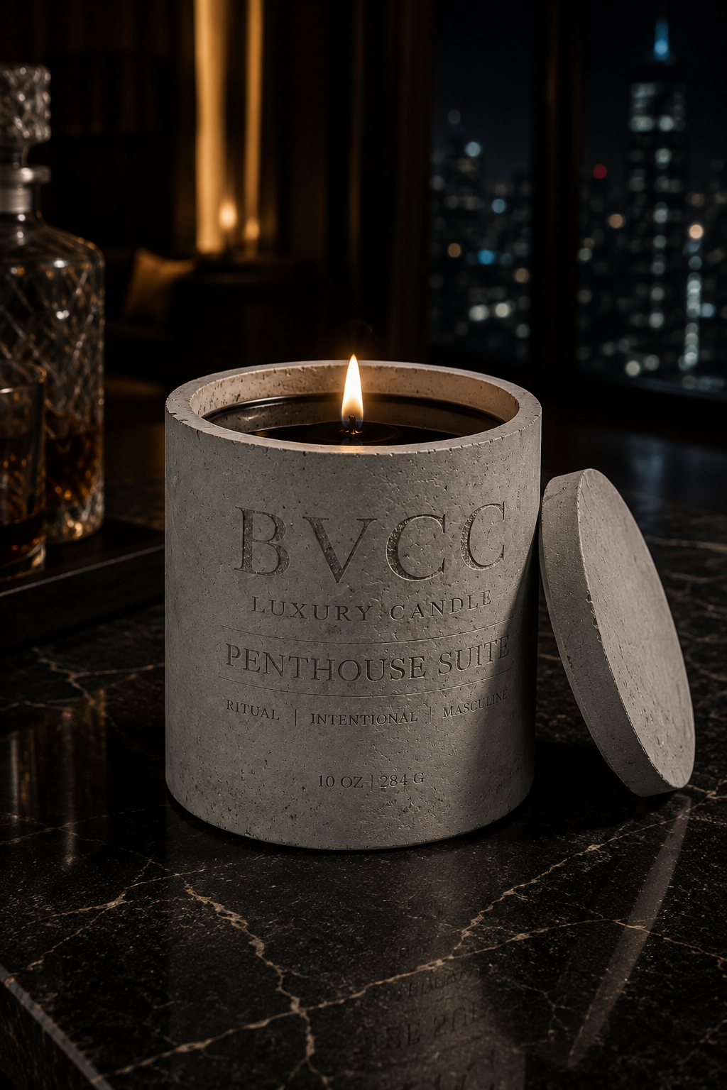 A lit luxury candle in a textured concrete container with the label 'BVCC Luxury Candle Penthouses Suite' on a black marble surface, with city lights visible through a window in the background.