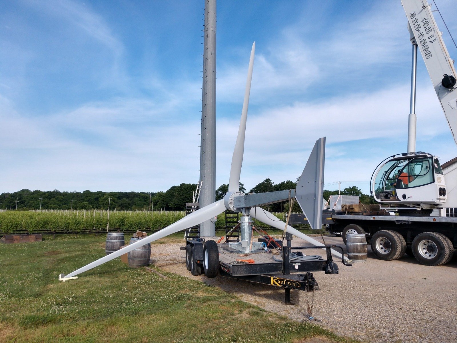 Un aerogenerador en proceso de montaje en un campo. Incluye una torre, palas y maquinaria en un camión y base para instalación.