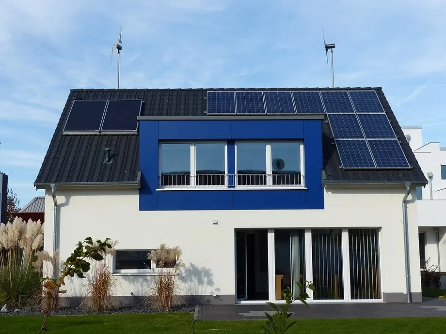 Casa moderna con paneles solares en el techo y tres aerogeneradores, en un día soleado.