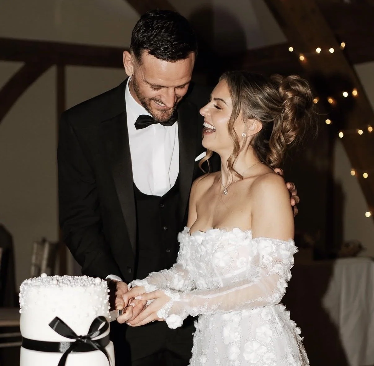 A bride and groom, dressed in wedding attire, smiling as they cut their wedding cake together.