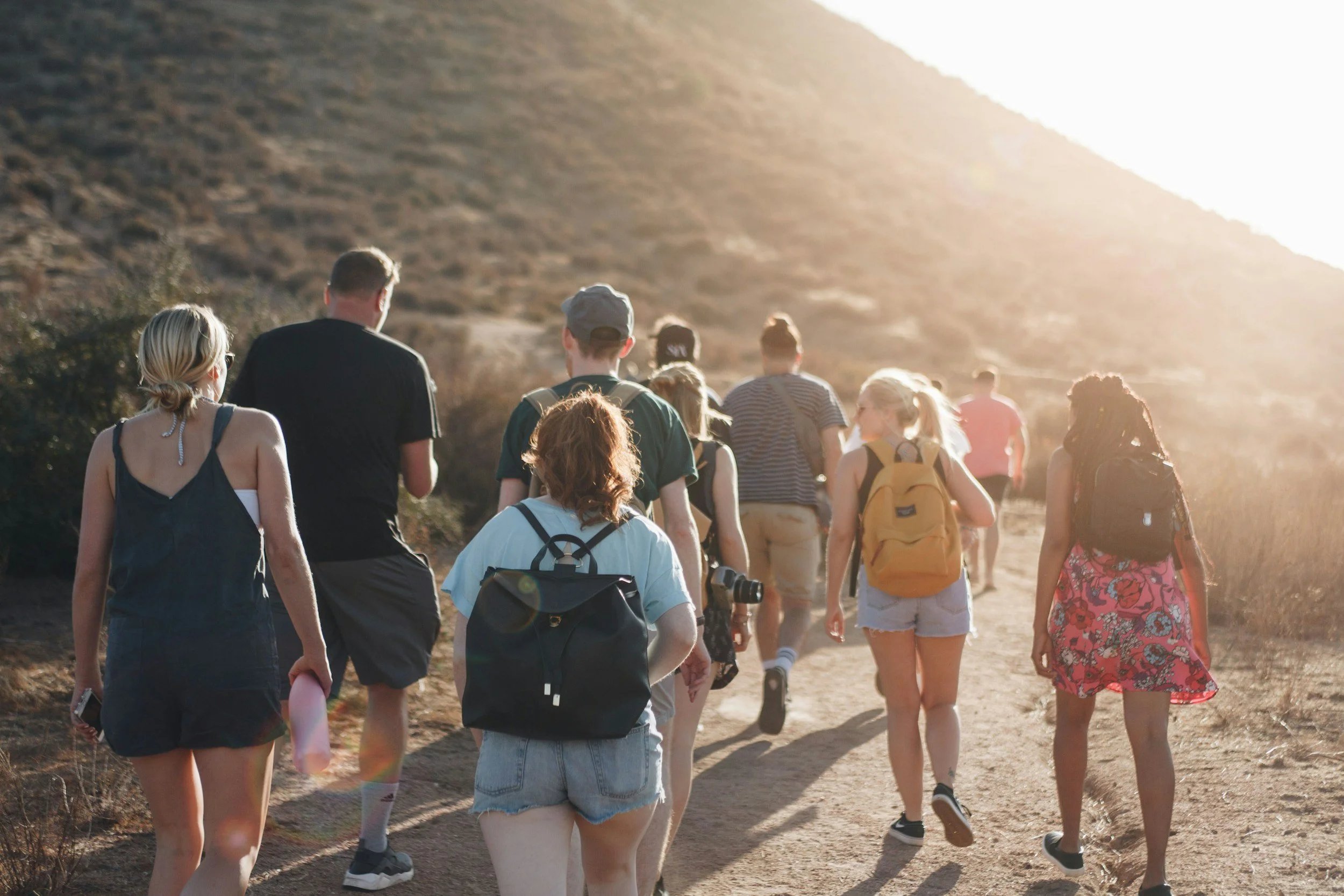 Group of people hiking on a trail in a desert-like landscape during sunset.
