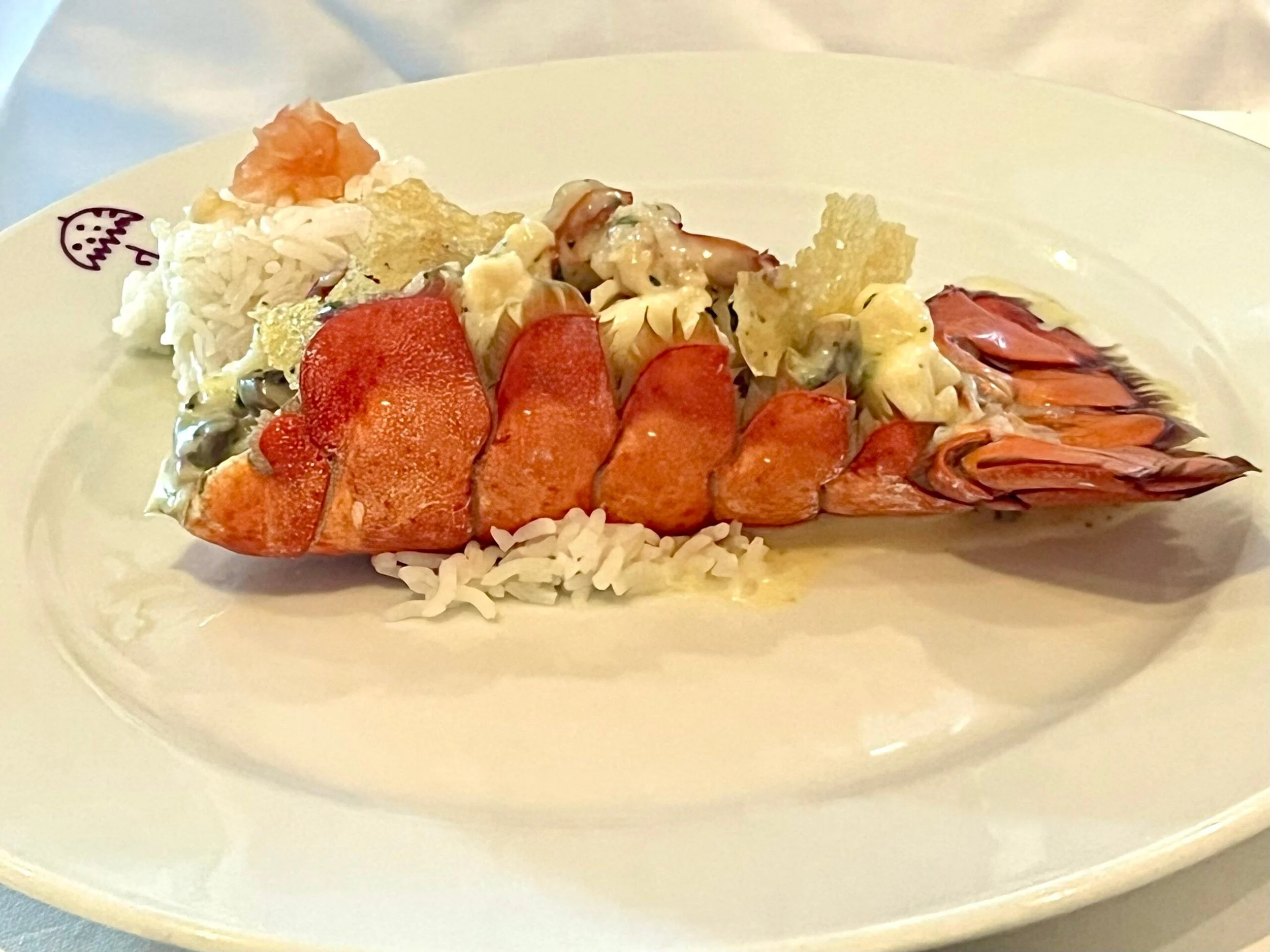 Lobster tail served on a white plate with rice and garnished with a small fruit piece.