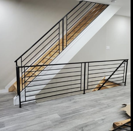 Interior view of a staircase with black metal railing, wood steps, and light-colored walls and flooring.