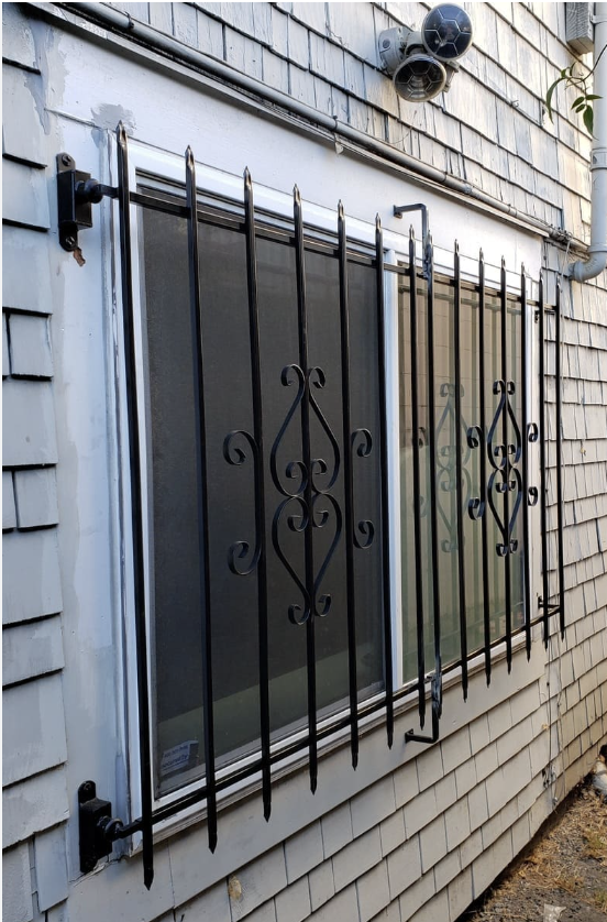 A window with black iron security bars installed outside, attached to a building with beige shingle siding.