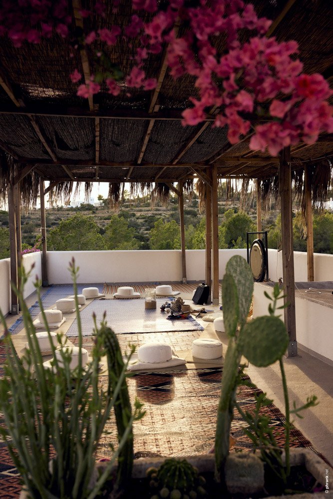 Ein offen gestalteter Dachgarten mit Kissen und Teppichen, umgeben von Pflanzen und einem Holz-Pergola, mit einer weiten Aussicht auf die Natur im Hintergrund.