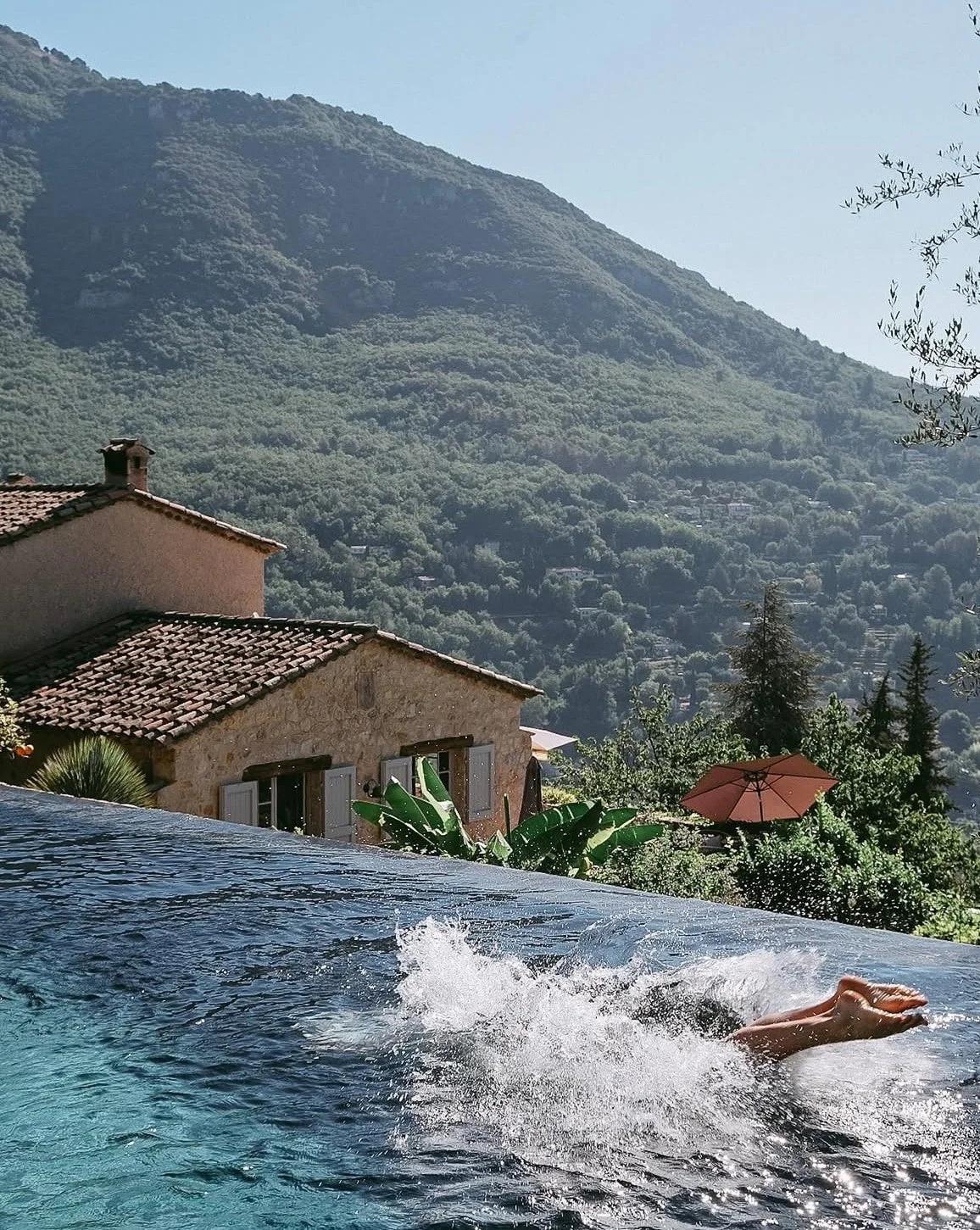 Ein Pool mit Blick auf ein Haus mit Terrakottadach und umliegender Natur inmitten von Bergen.