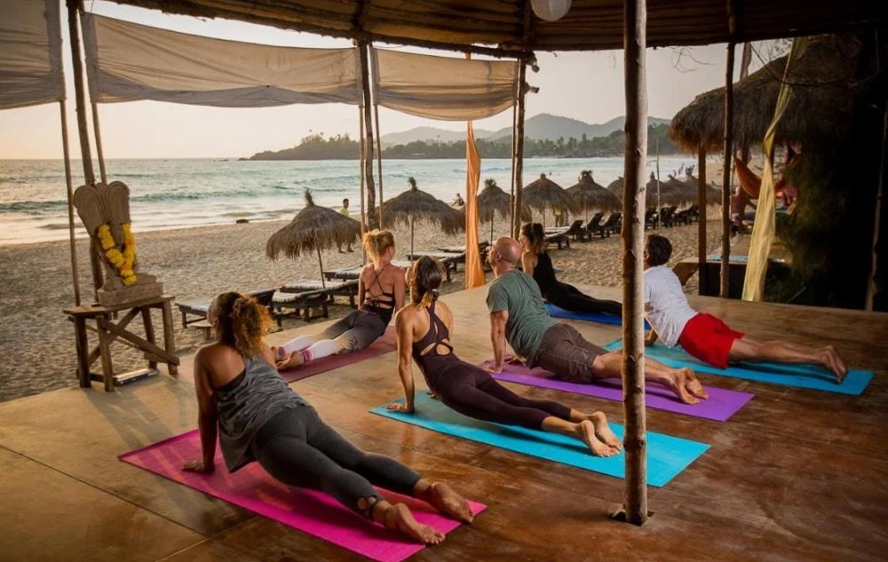 Menschen beim Yoga am Strand an einem Unterstand bei Sonnenuntergang.