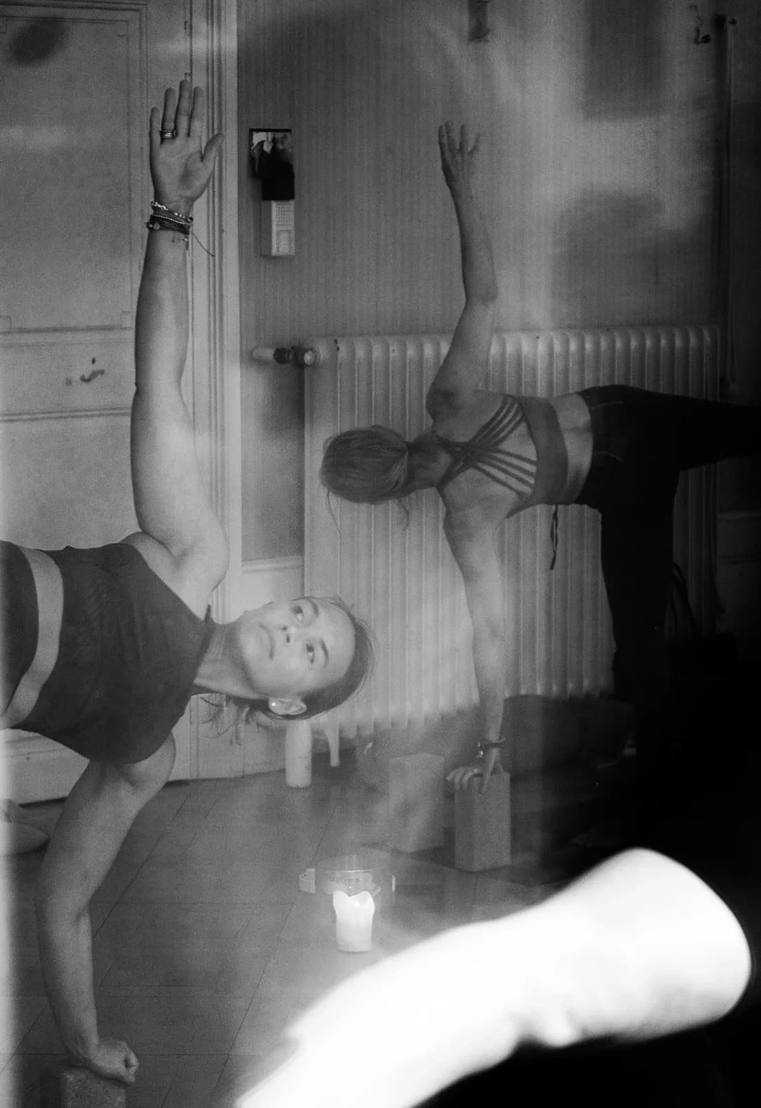 Zwei Frauen machen Yoga im Raum, eine im Front- und eine im Side-View, bei schwachem Licht, mit Kerzen auf dem Boden.