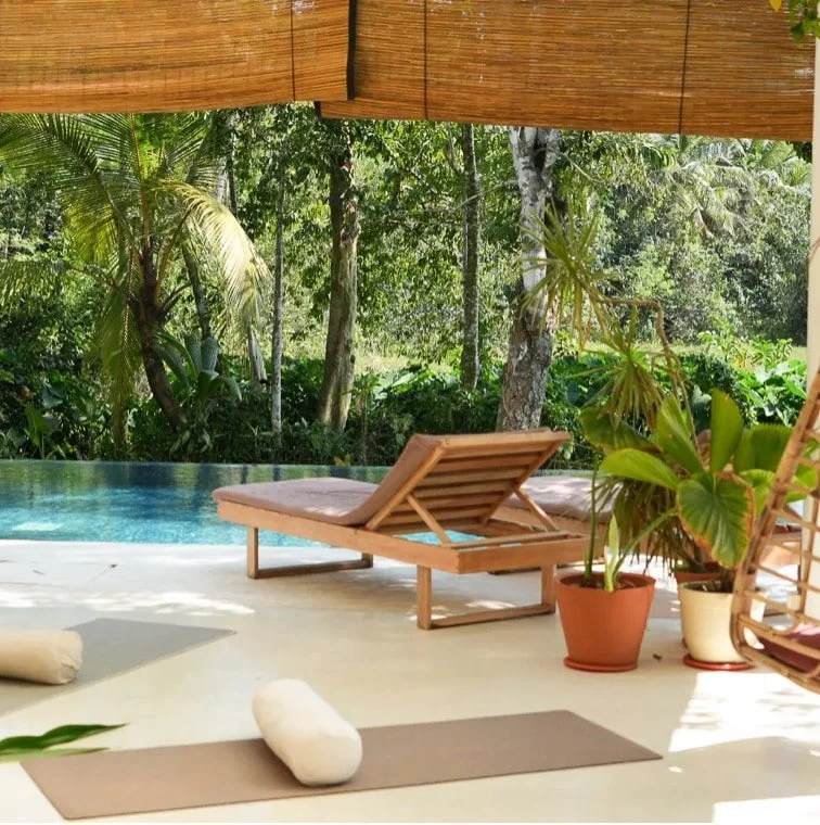 Entspannter Außenbereich mit Pool, Liegestuhl, Yoga-Matten, Pflanzen und Blick in den grünen Garten unter Sonnenschirm