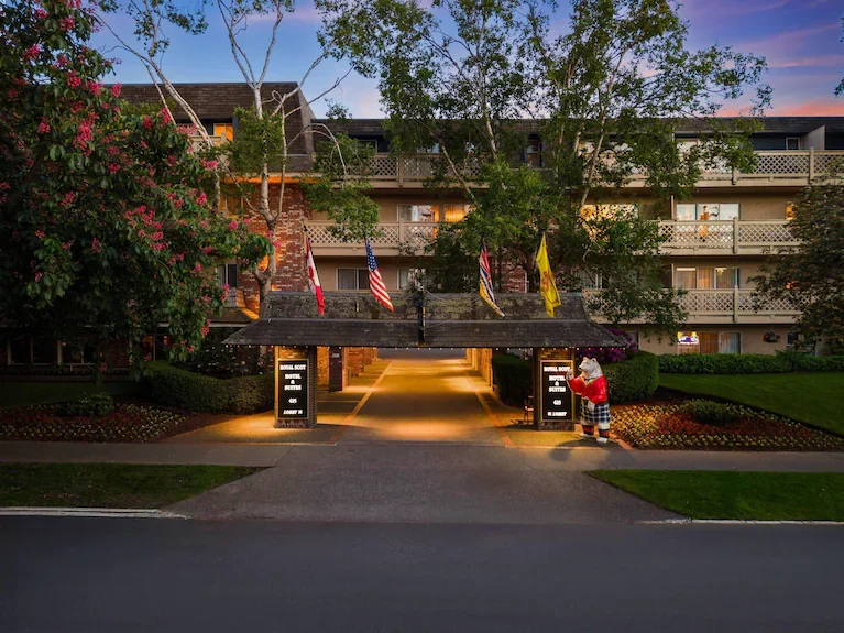 Entrance to a hotel with a covered walkway, flags, and a mascot figure near the right side.