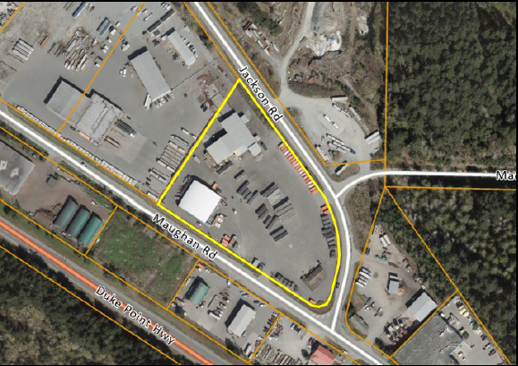 Aerial view of an industrial area with buildings, storage yards, and parking lots near Duke Point Highway, with roads Jackson Road and Maughan Road marked.