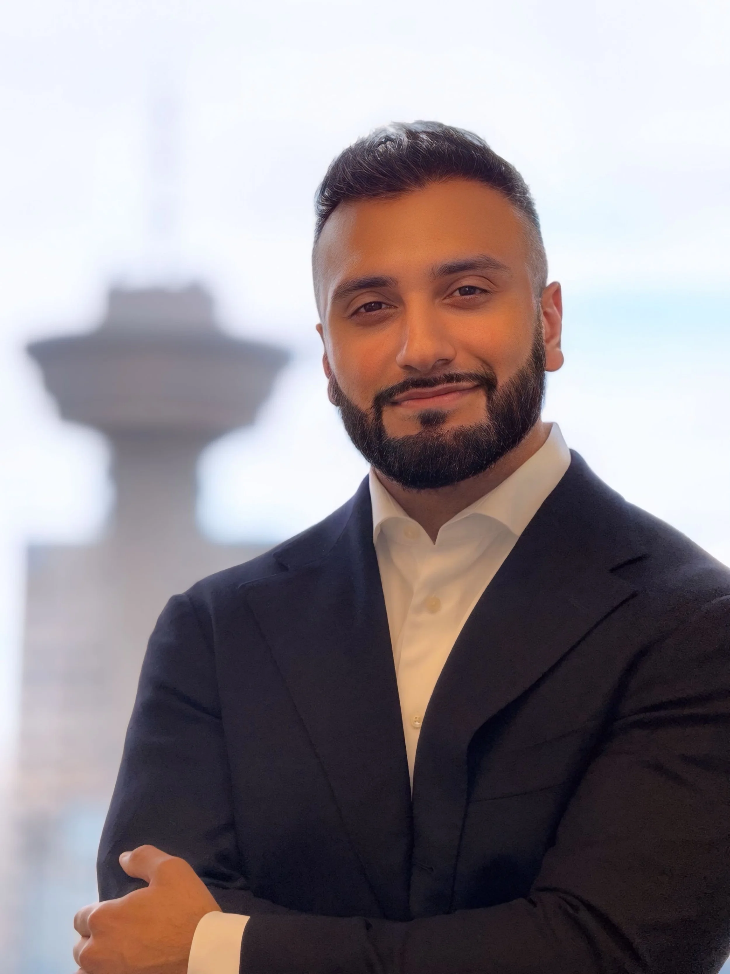 A man in formal attire, smiling, with a blurred background featuring the Space Needle in Seattle.