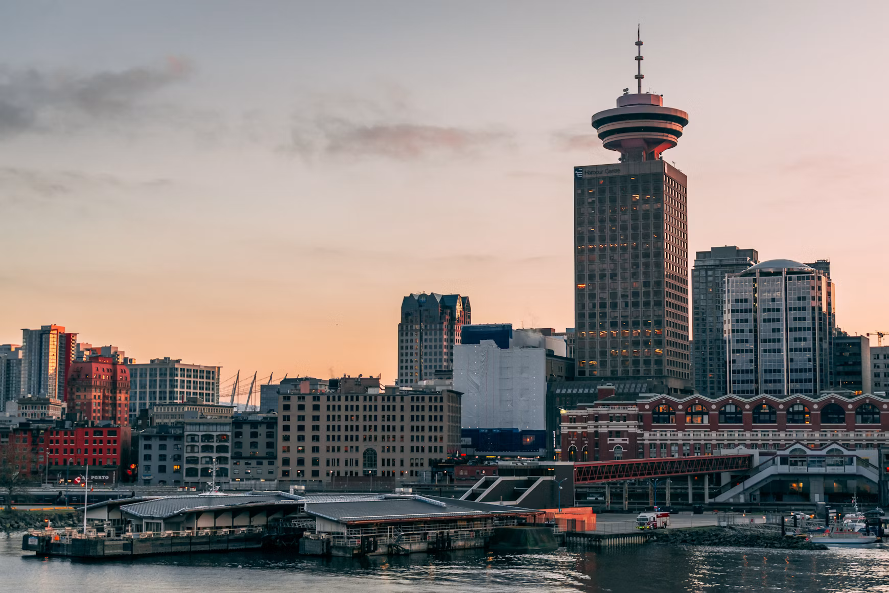 Skyline of Vancouver, British Columbia, featuring the Harbour Centre tower at sunset with a calm river in the foreground.