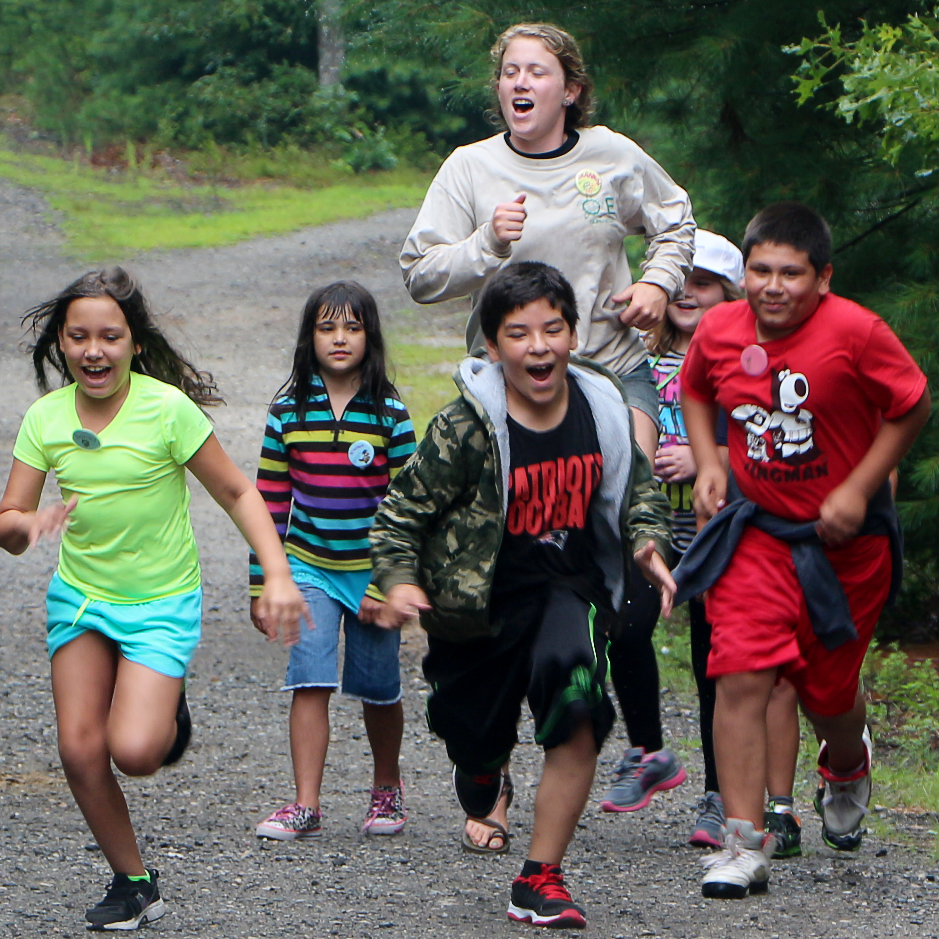 Group of children and teenagers running outdoors on a gravel path surrounded by greenery and trees.