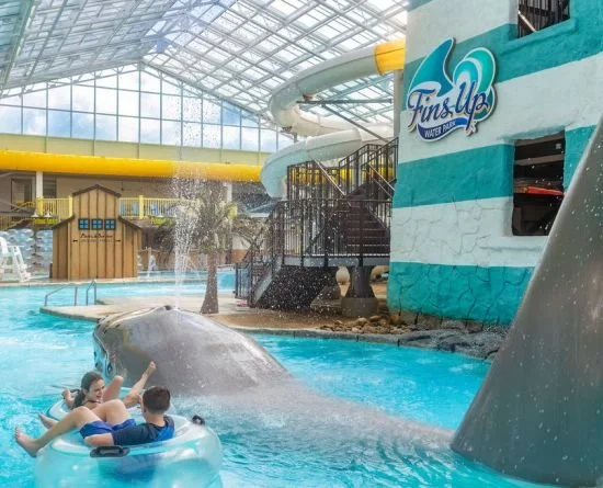 Indoor water park featuring a splash area with a whale-shaped water slide, a yellow tube slide, and a group of children in a circular pool