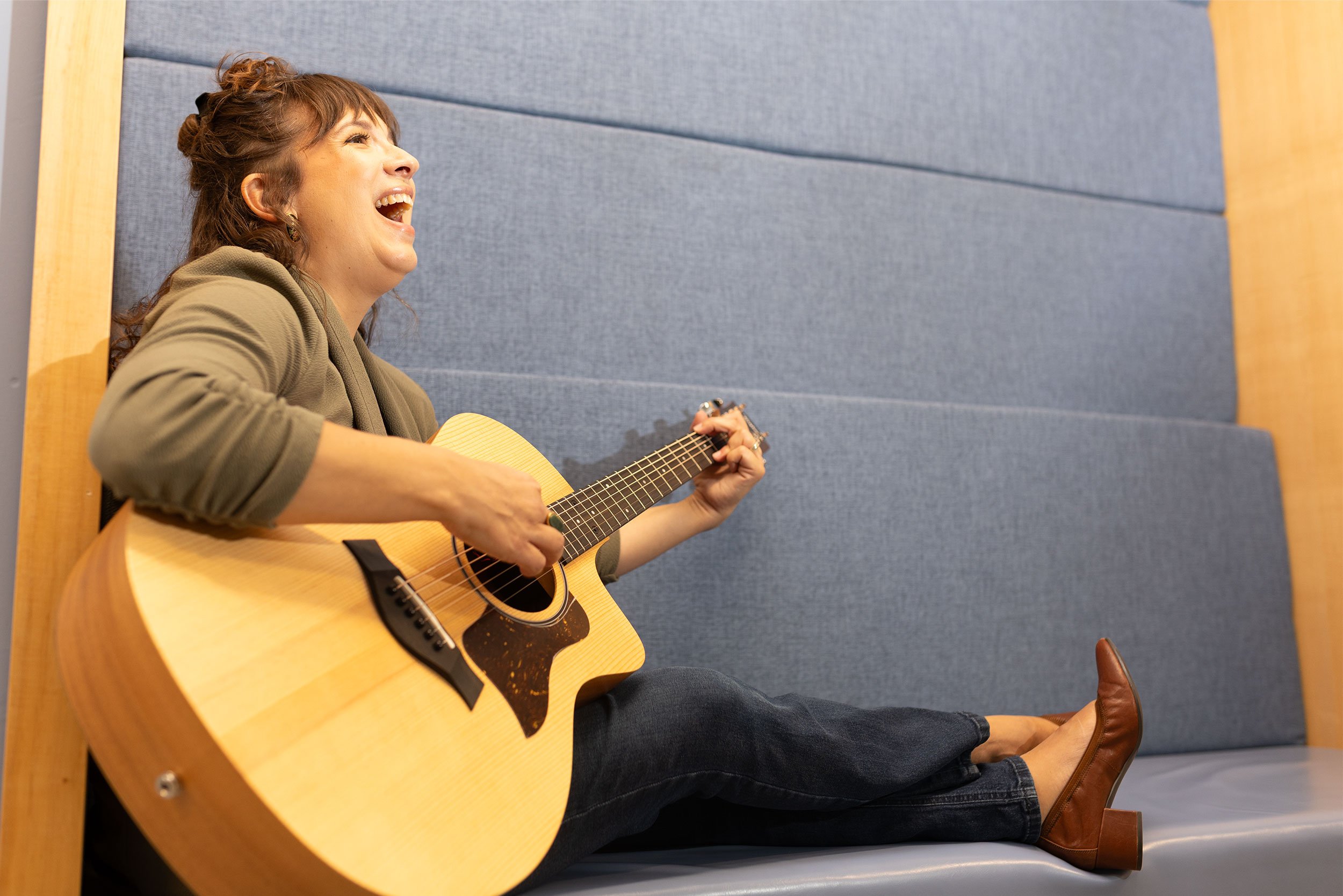 Sarah Keely Decker playing guitar, seated on a bench.