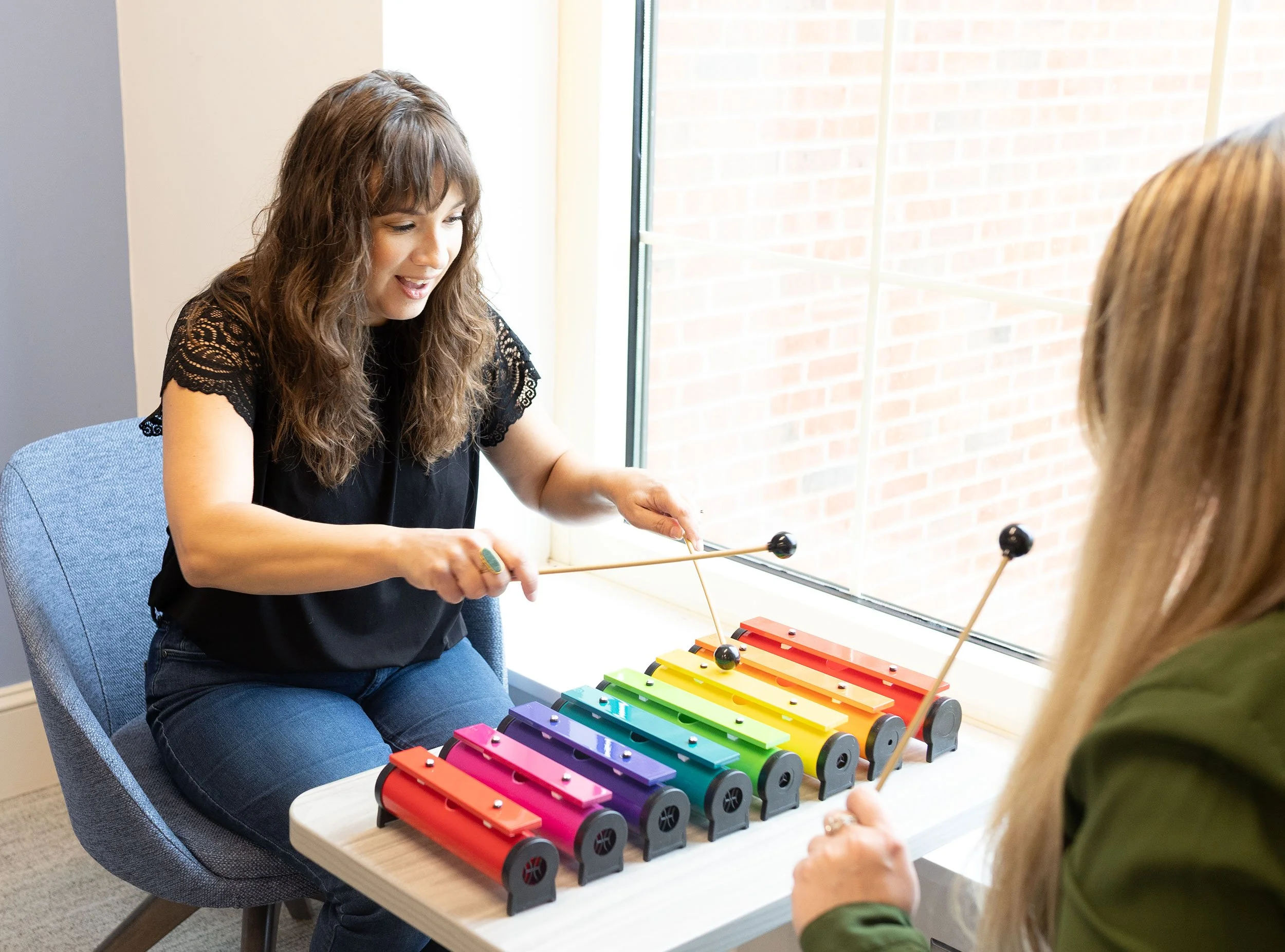 Sarah Keely Decker and a client playing colorful bells together indoors.