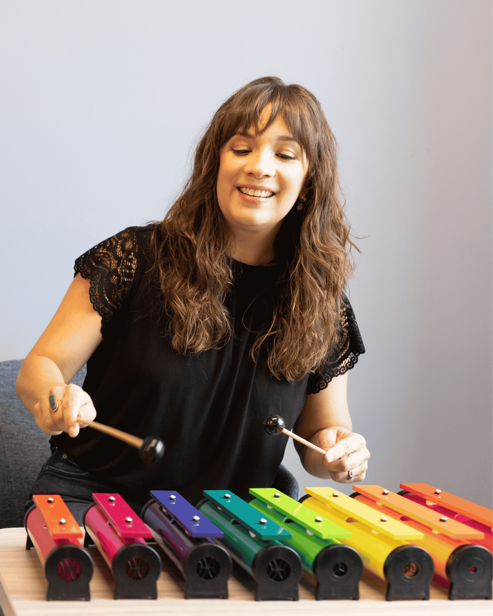 Sarah Keely Decker, board-certified music therapist, smiling while playing colorful tone bells with mallets.Sarah Keely Decker, board-certified music therapist, smiling while playing colorful tone bells with mallets.