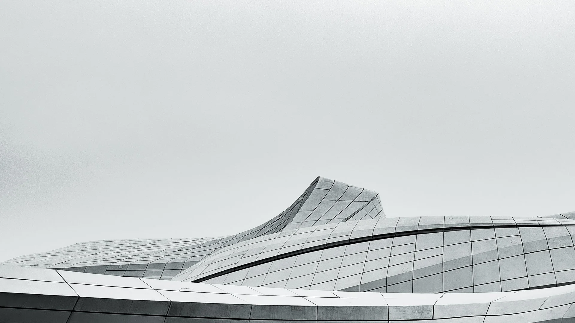 Modern architectural building with a sleek, curved design and metallic exterior, set against a cloudy sky.