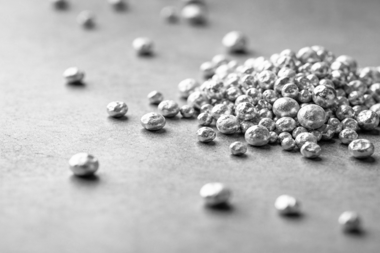 Silver-colored nuggets scattered on a flat surface, with a pile of nuggets in the background.