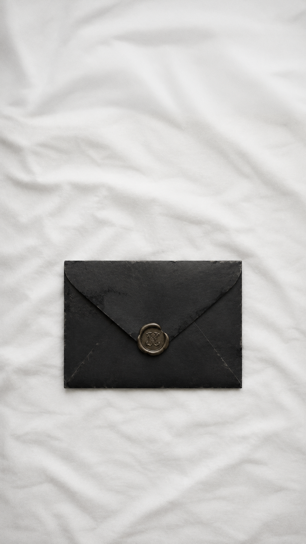 A closed black envelope with a wax seal on top of a white fabric surface.