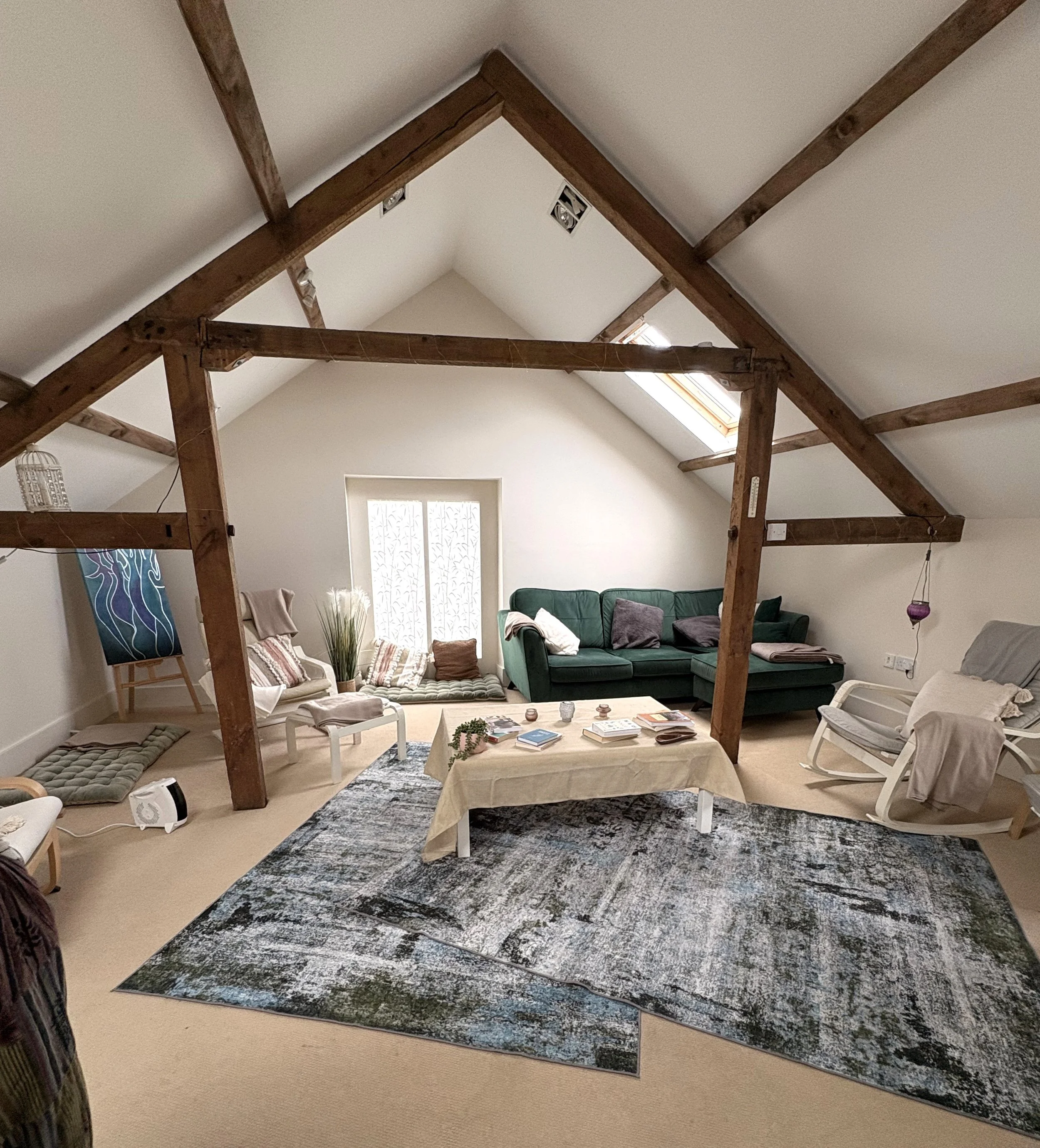 Living room with wooden beams on the ceiling, green sofa, chairs, coffee table, and a large oriental rug. Skylight and window letting in natural light.