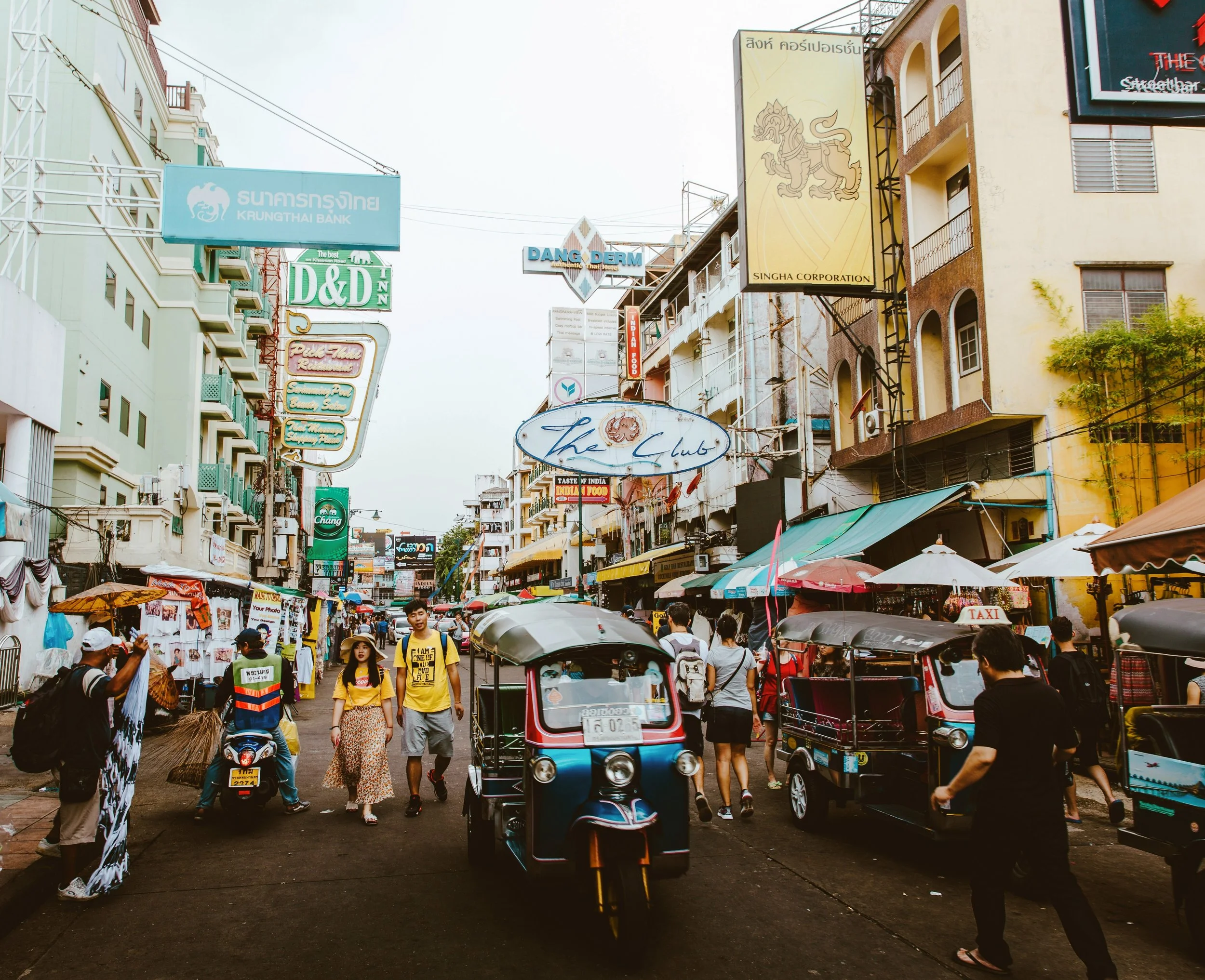 Busy street with signs, tuk-tuks and pedestrians in a lively neighborhood, Banglamphu, Bangkok.