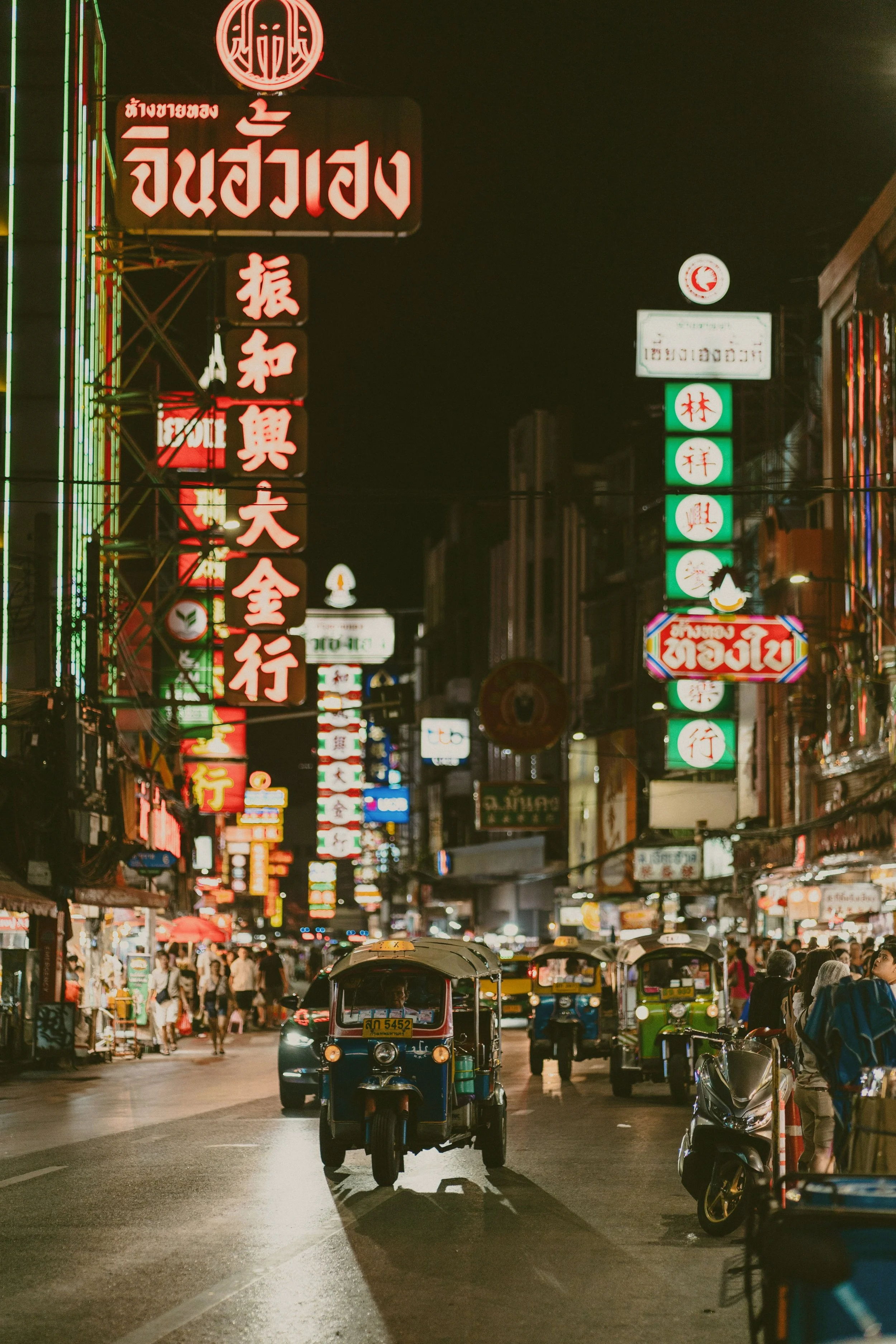 Neon signs lighting up a busy street at night with traffic and pedestrians, Yaowarat Road, Chinatown, Bangkok.