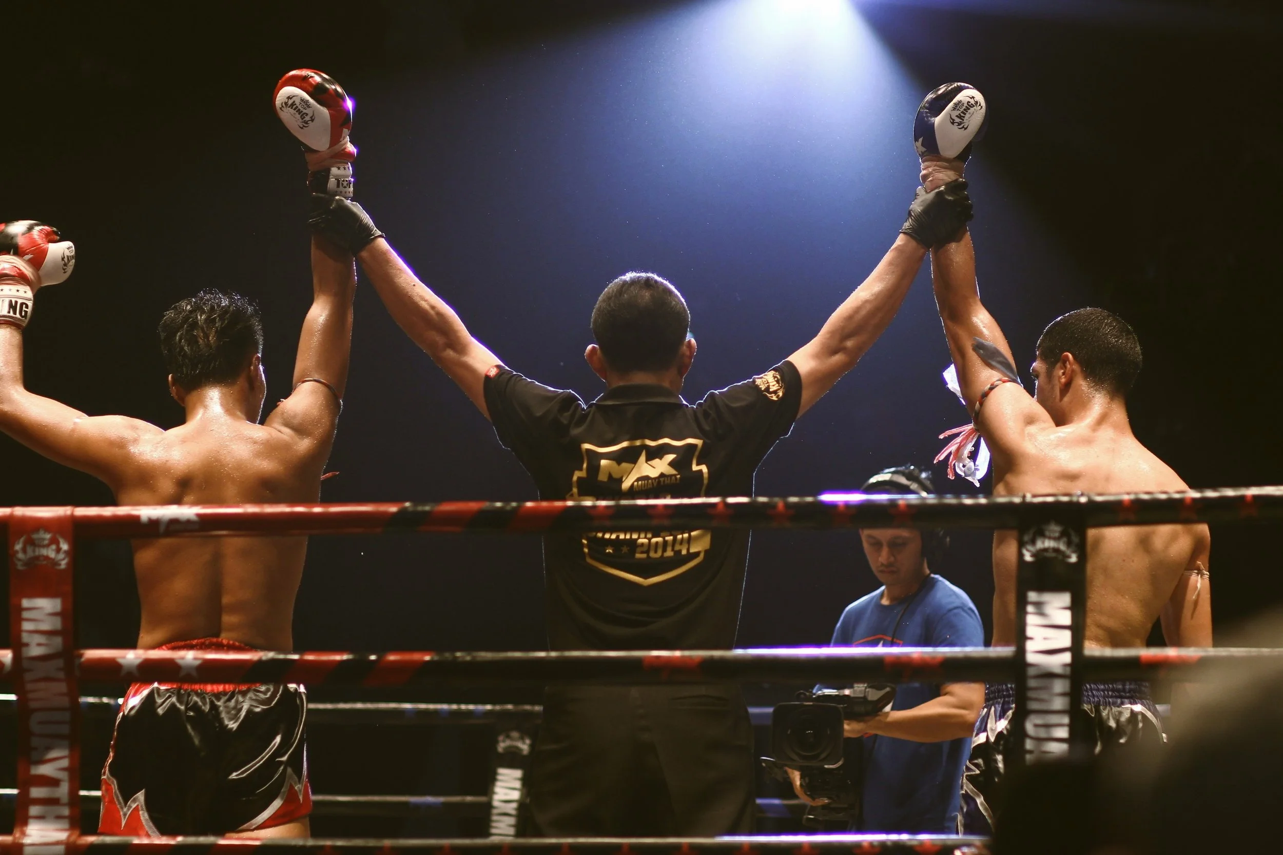 Muay Thai fighters in a ring raising their hands in victory after a match.
