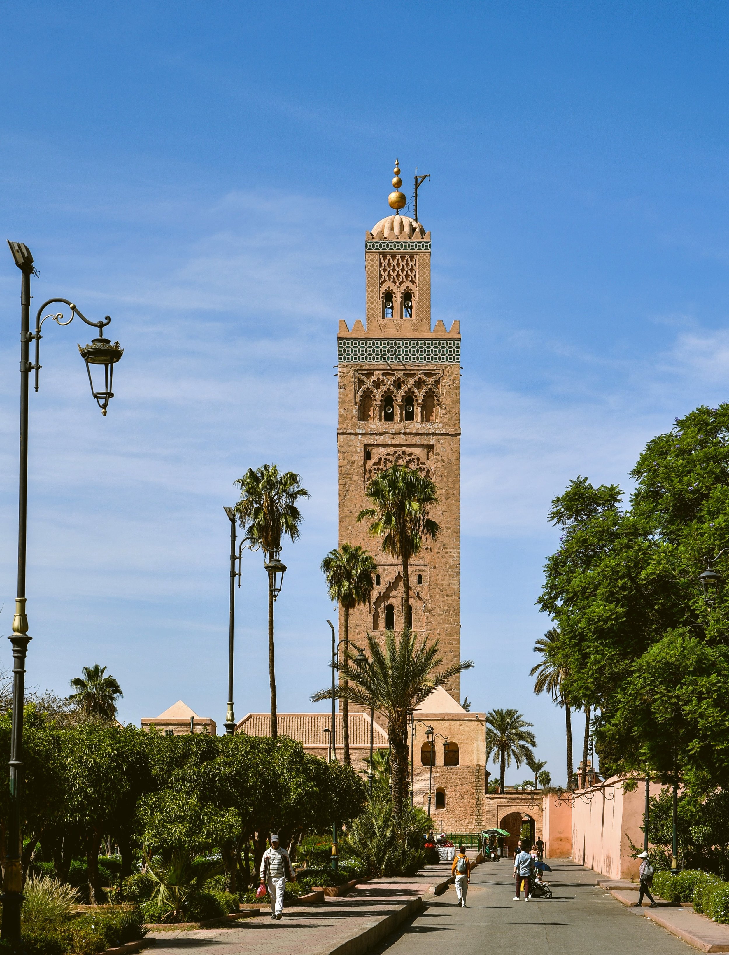 Koutoubia Mosque minaret rising above palm trees and gardens under a clear blue sky, Marrakech.