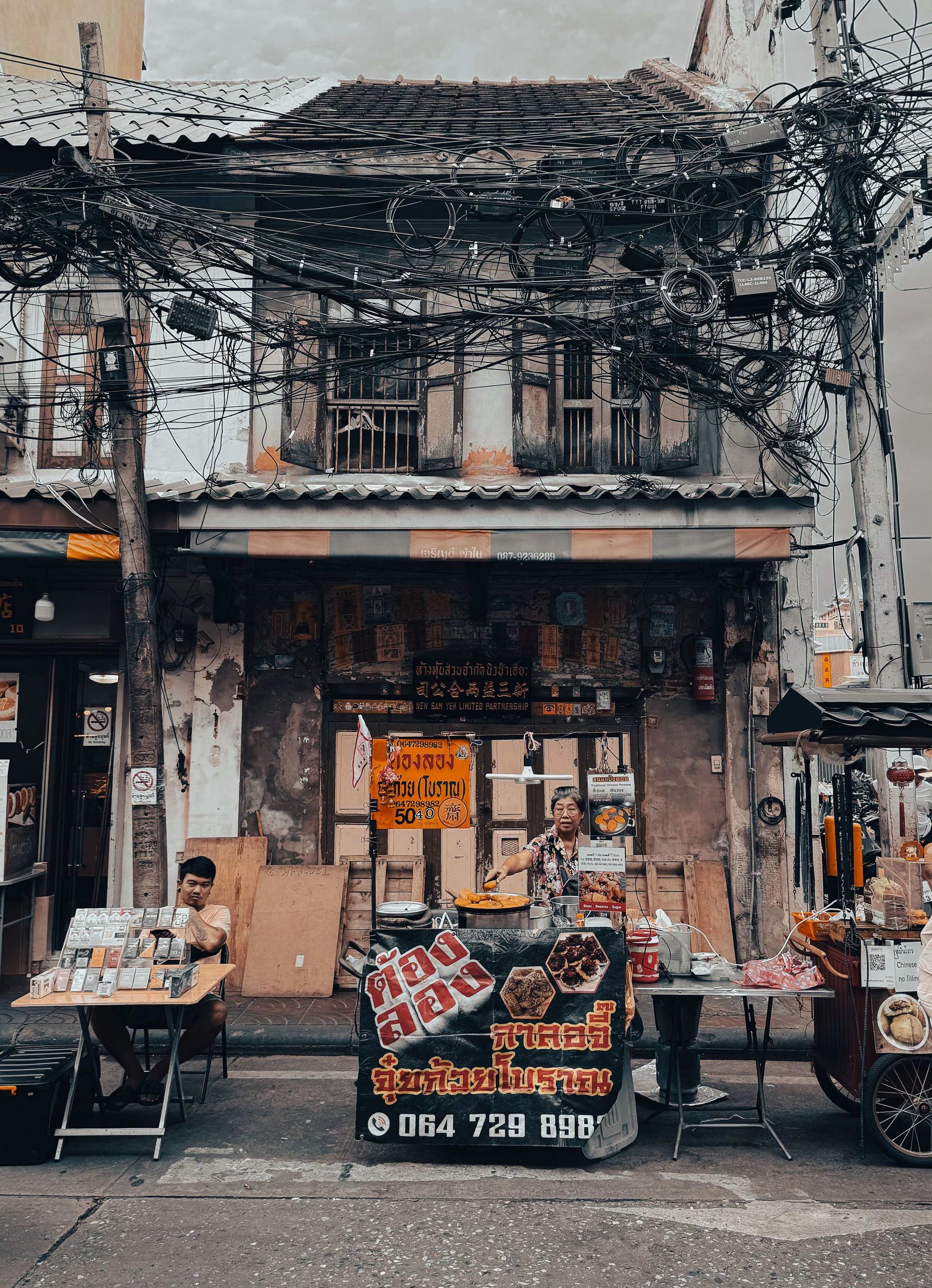 Old shophouse with a weathered facade and tangled overhead wires above a street food stall, Bangkok.