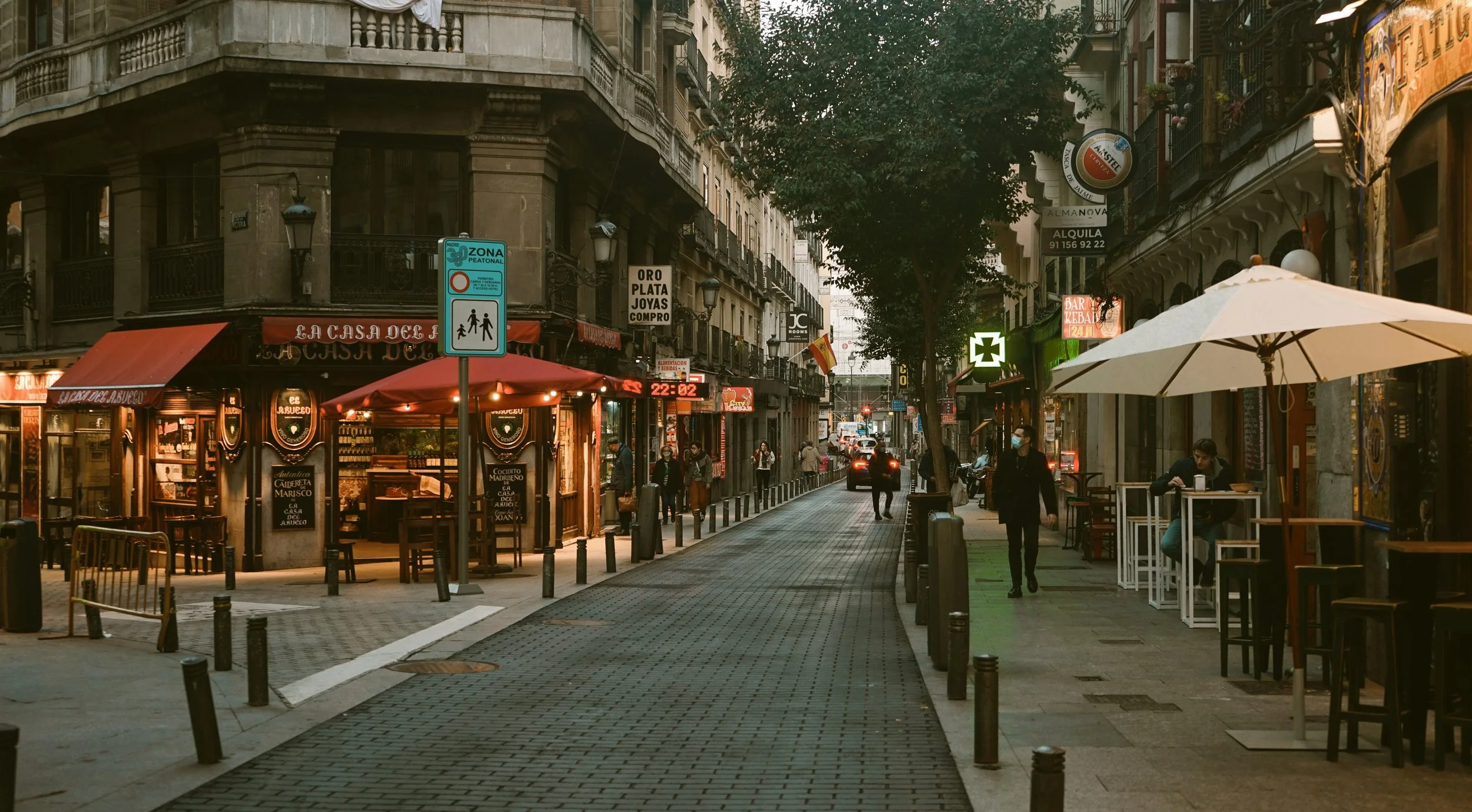 Evening light on a lively street with outdoor tables and umbrellas in central Madrid