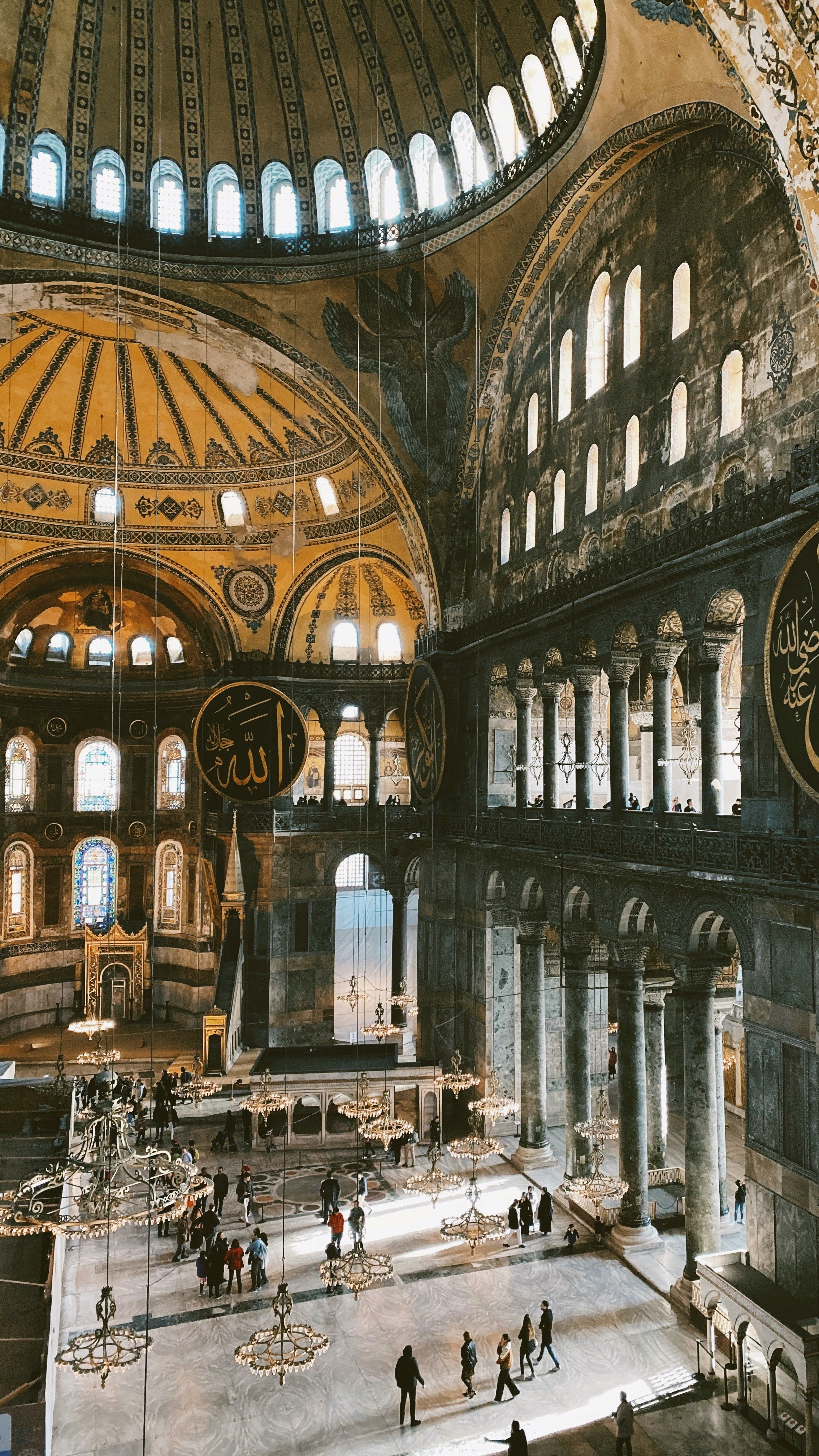 Interior of Hagia Sophia with its central dome, golden mosaics and visitors on the marble floor, Istanbul.