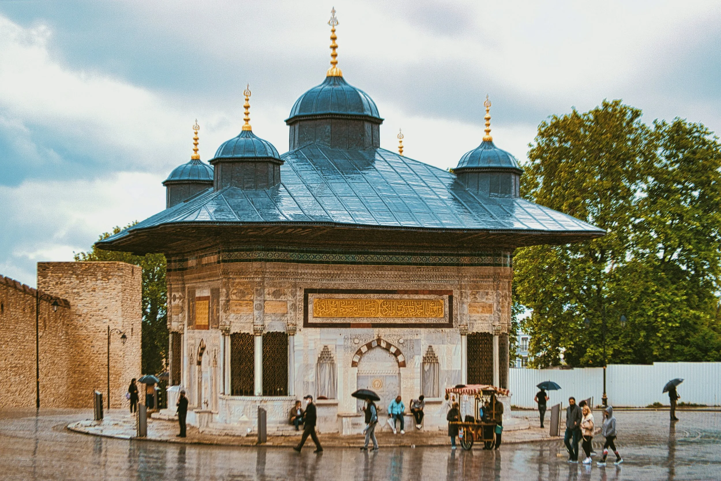 Ottoman fountain pavilion with blue-gray domes, ornate stone walls and a gilded inscription, Topkapı Palace, Istanbul.