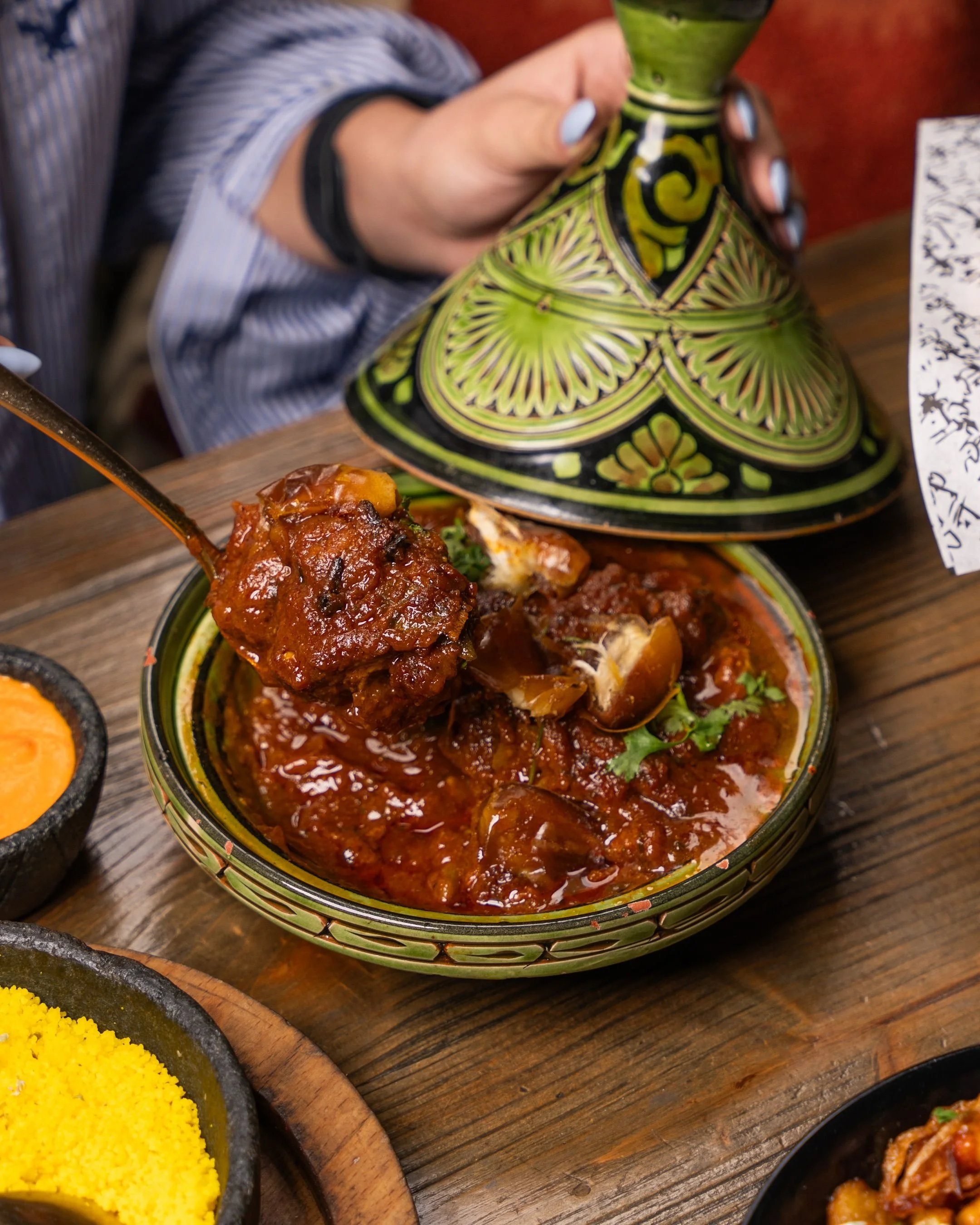 Tagine served in a green ceramic dish with a hand lifting the conical lid, Marrakech.