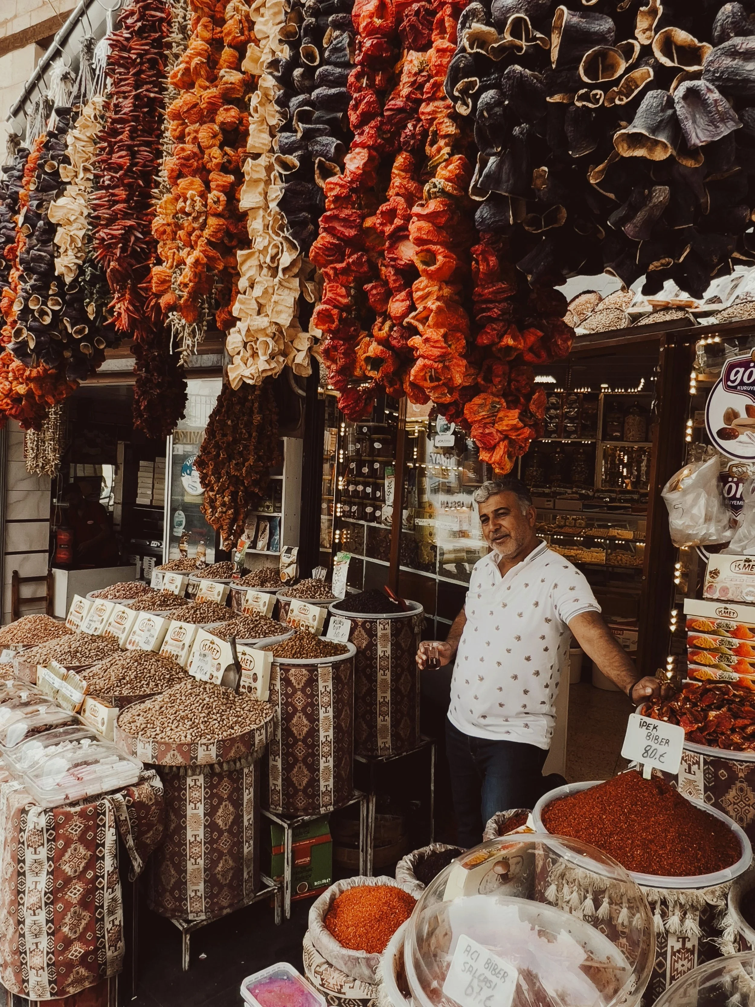 Spice Bazaar stall with strings of dried peppers hanging above jars and bowls of goods, with a vendor behind the counter, Istanbul