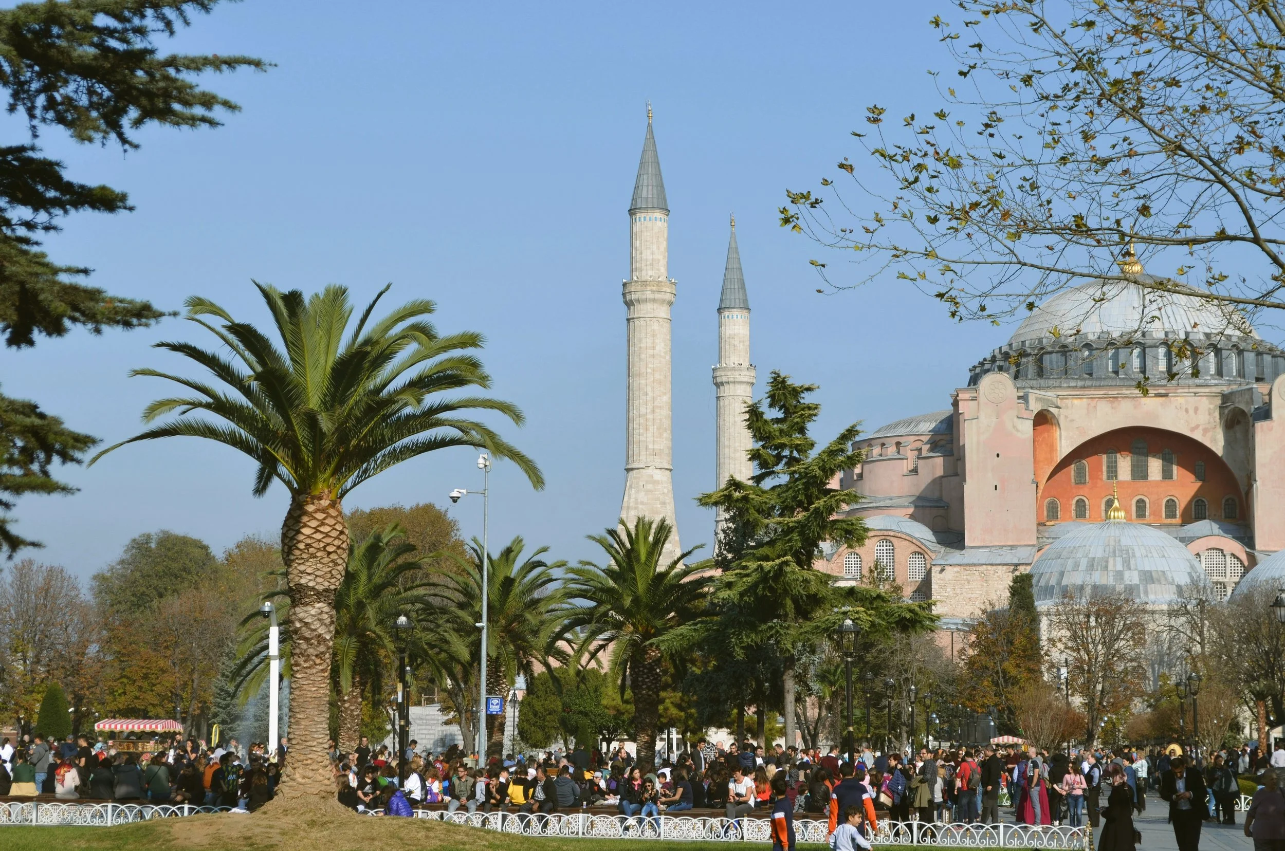 Hagia Sophia with its minarets rising behind palm trees and crowds of visitors in the square, Istanbul.