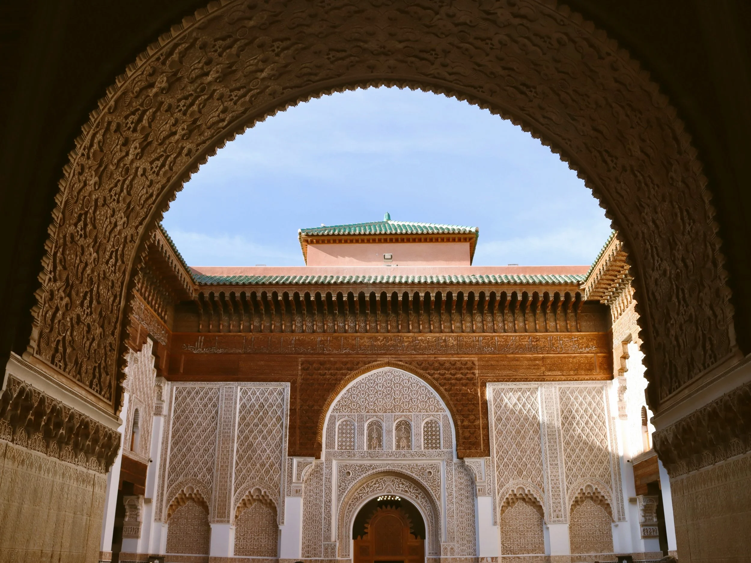 Ornate carved-cedar and stucco courtyard seen through a horseshoe arch, Ben Youssef Madrasa, Marrakech.