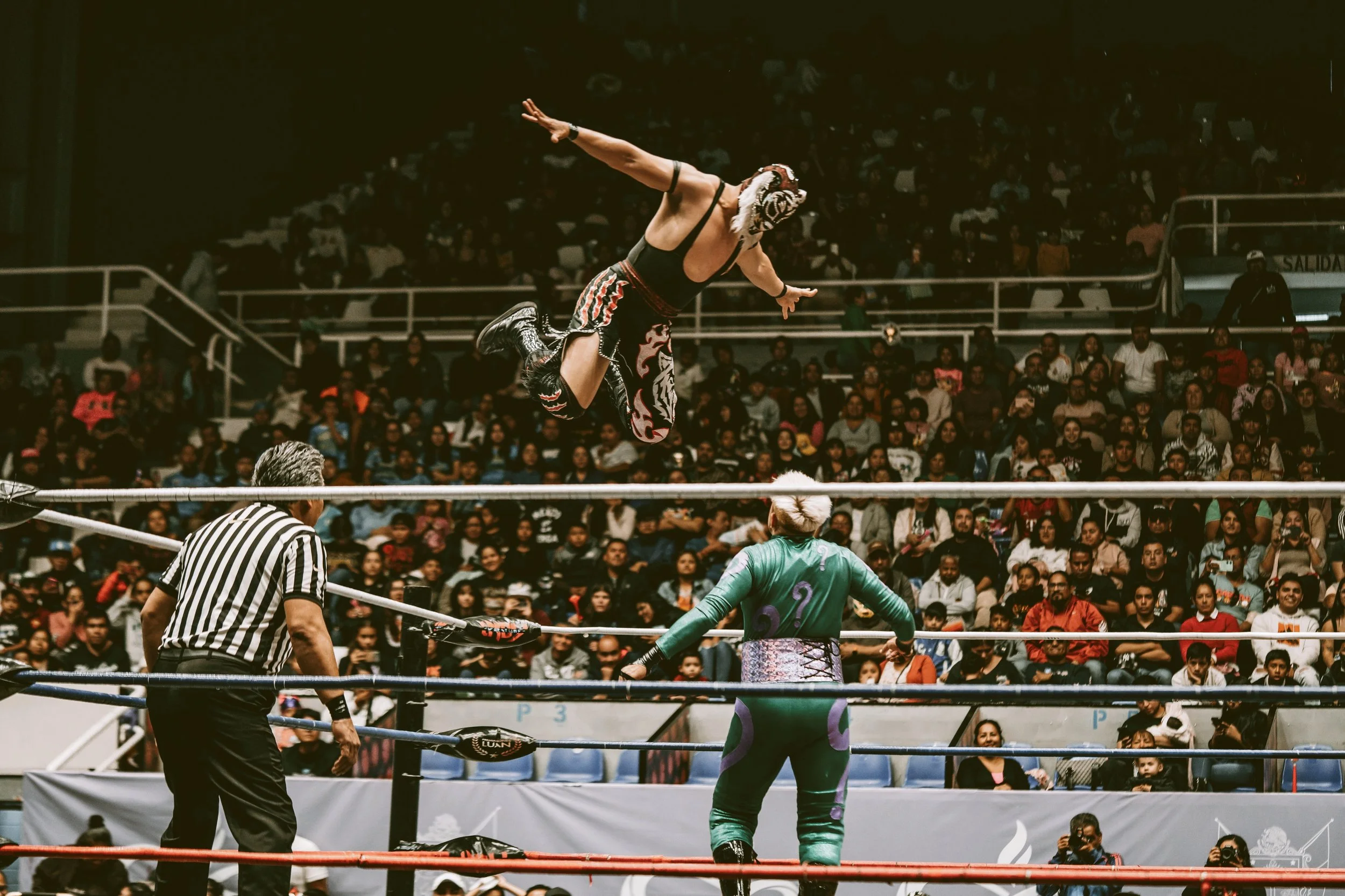 Lucha libre wrestler leaping from the top rope toward an opponent while a referee watches, Mexico City.