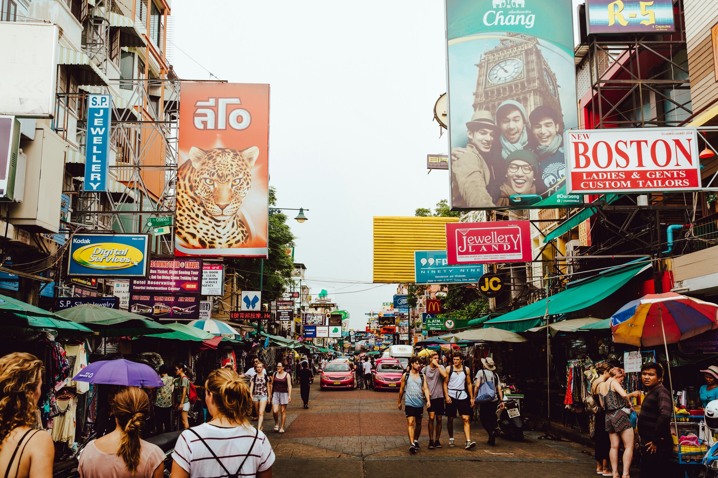 Busy street lined with colorful signs and billboards under awnings, Khao San Road, Bangkok.