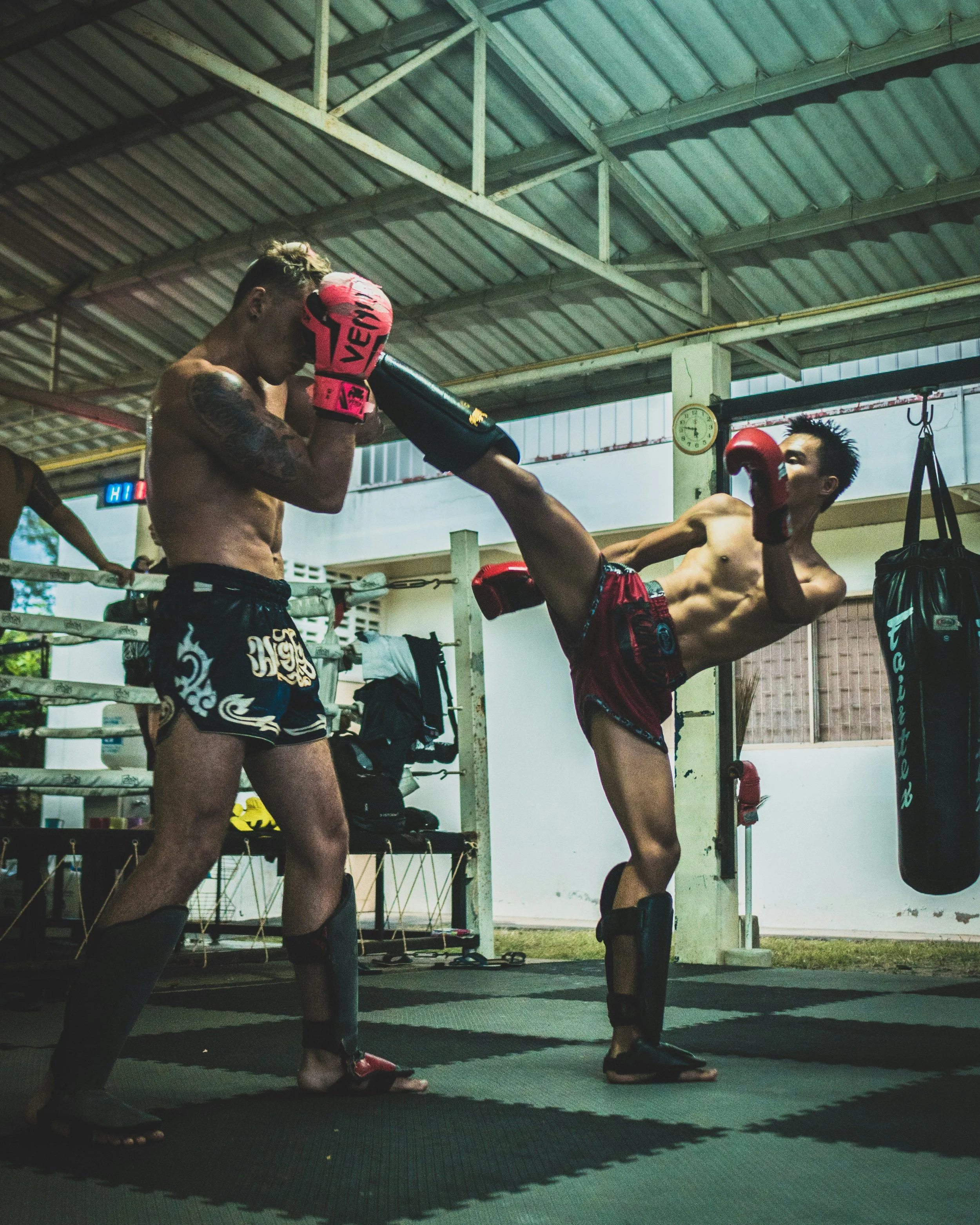Two shirtless men practicing Muay Thai boxing in a gym, Bangkok.