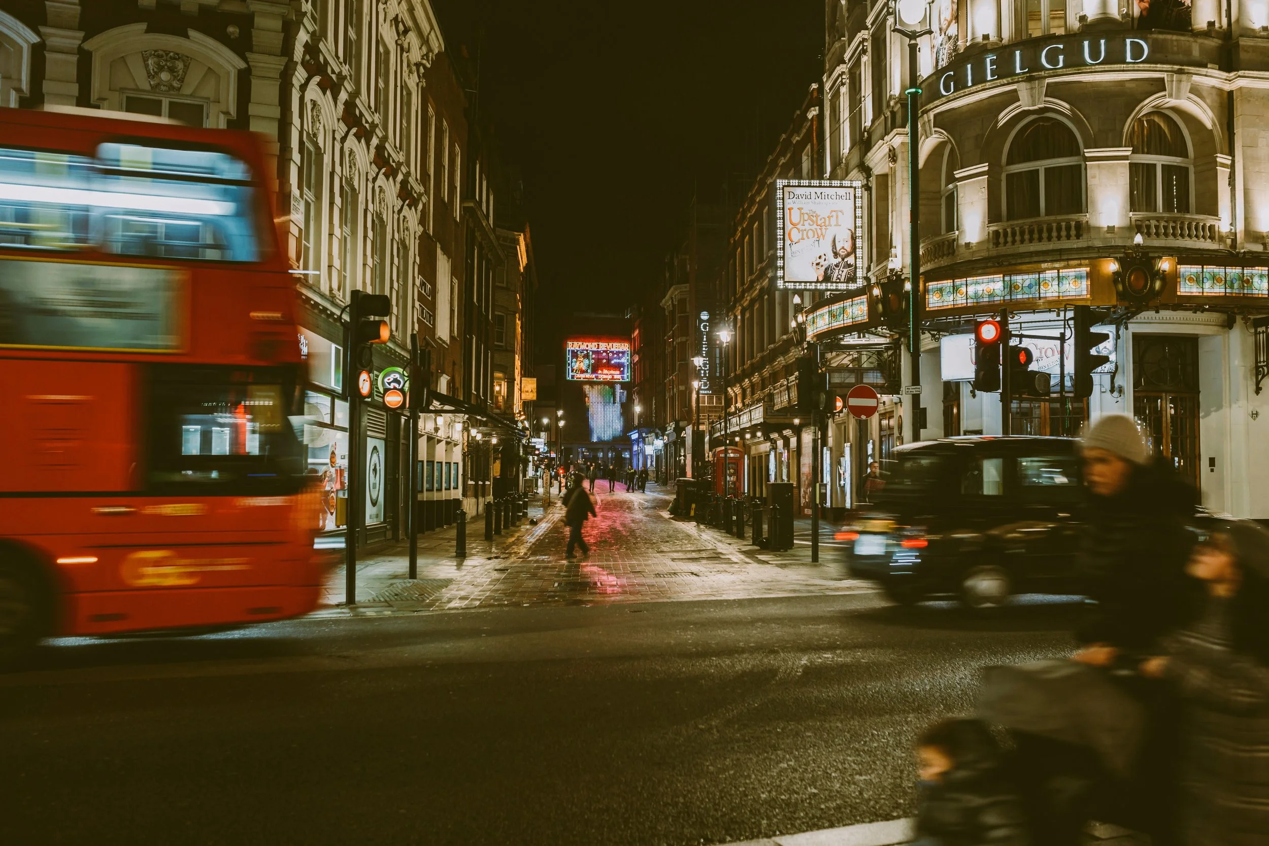 Blurred red double-decker bus on a busy street at night, London.
