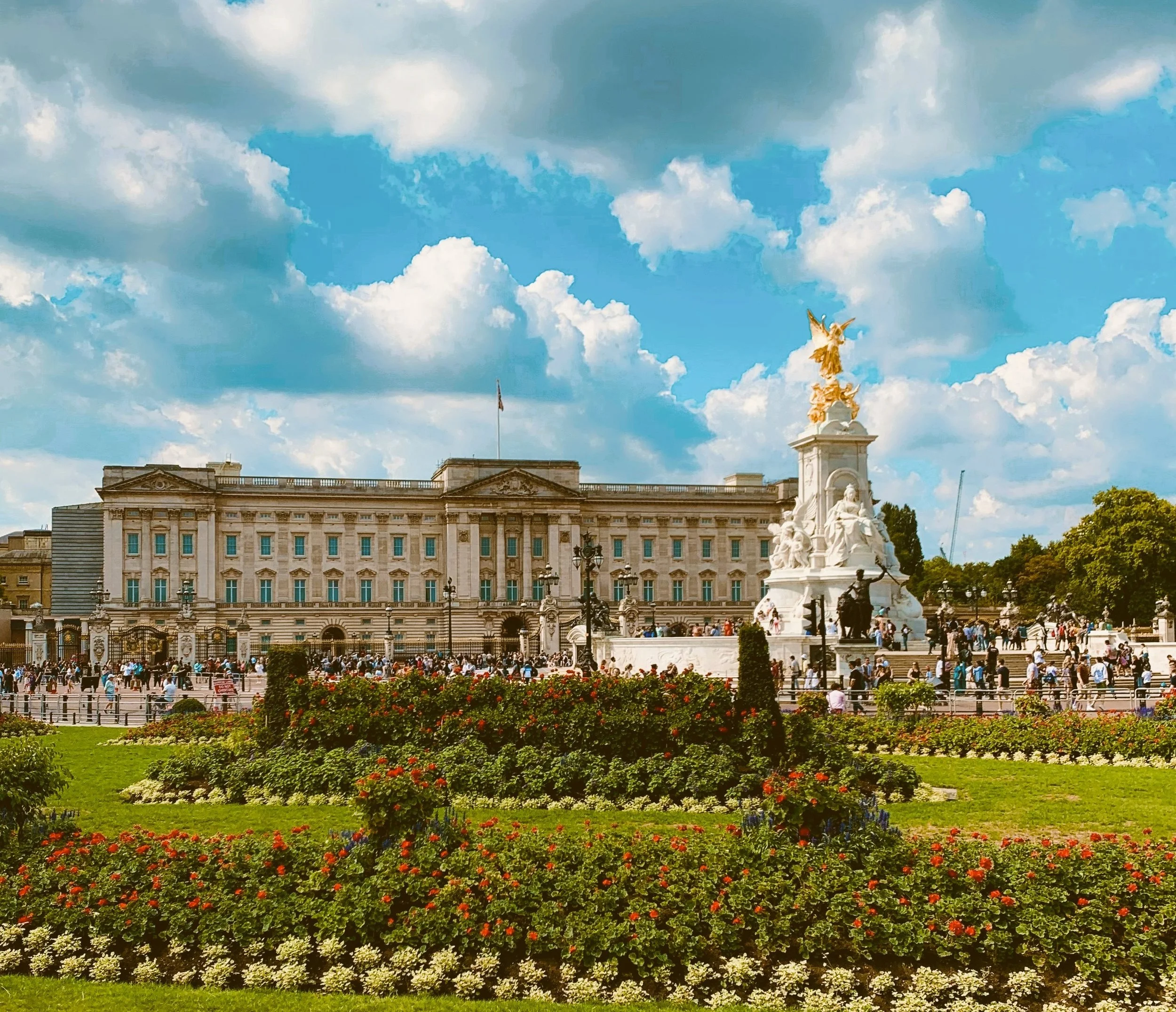 Buckingham Palace across the Victoria Memorial gardens under a blue sky with clouds, London.