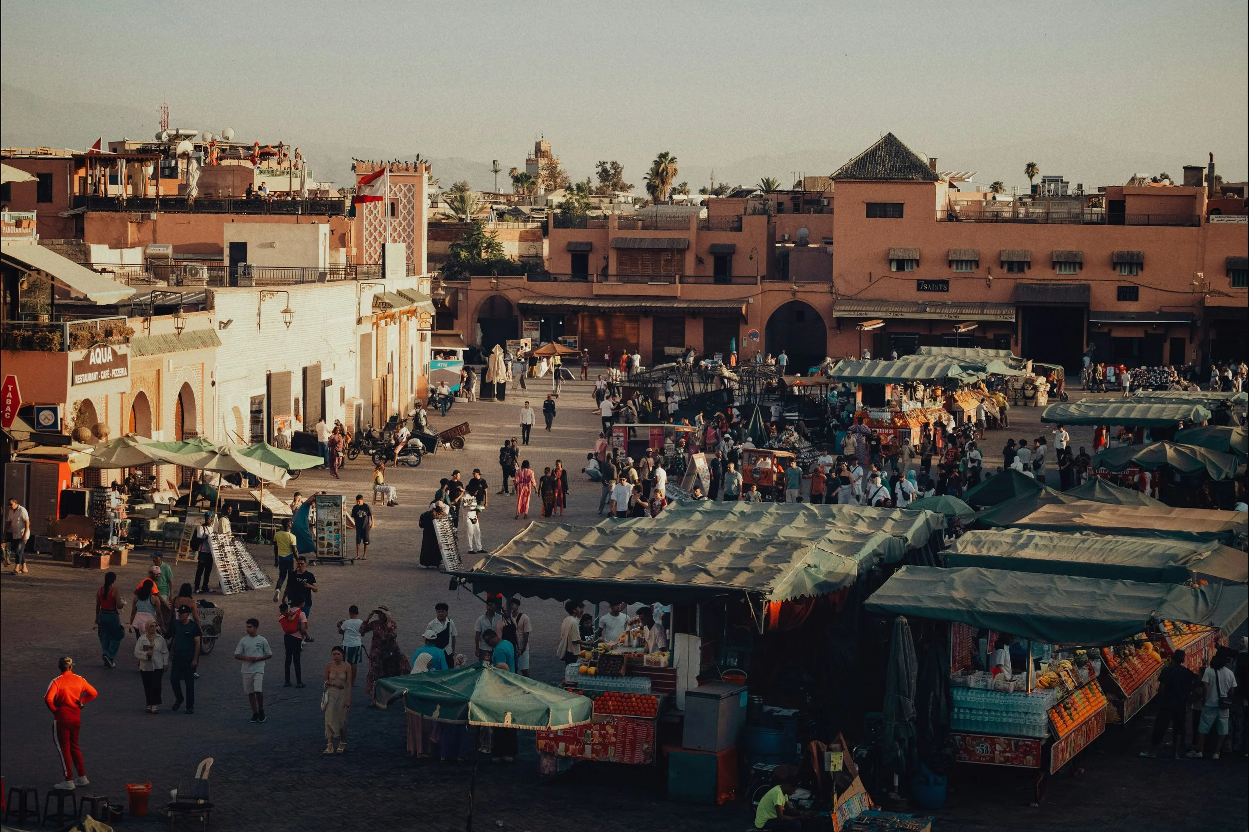 Rooftop view over Jemaa el-Fnaa square with market stalls and terracotta buildings in warm evening light, Marrakech.