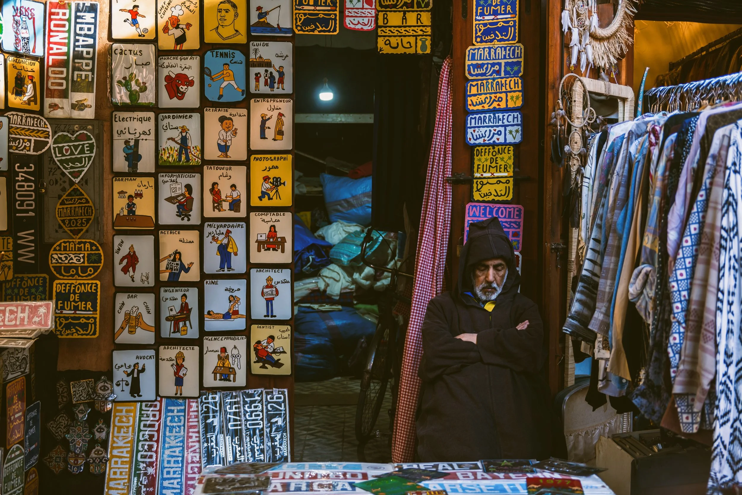 Souk shop with walls covered in postcards and posters and clothes hanging at the entrance, Marrakech.