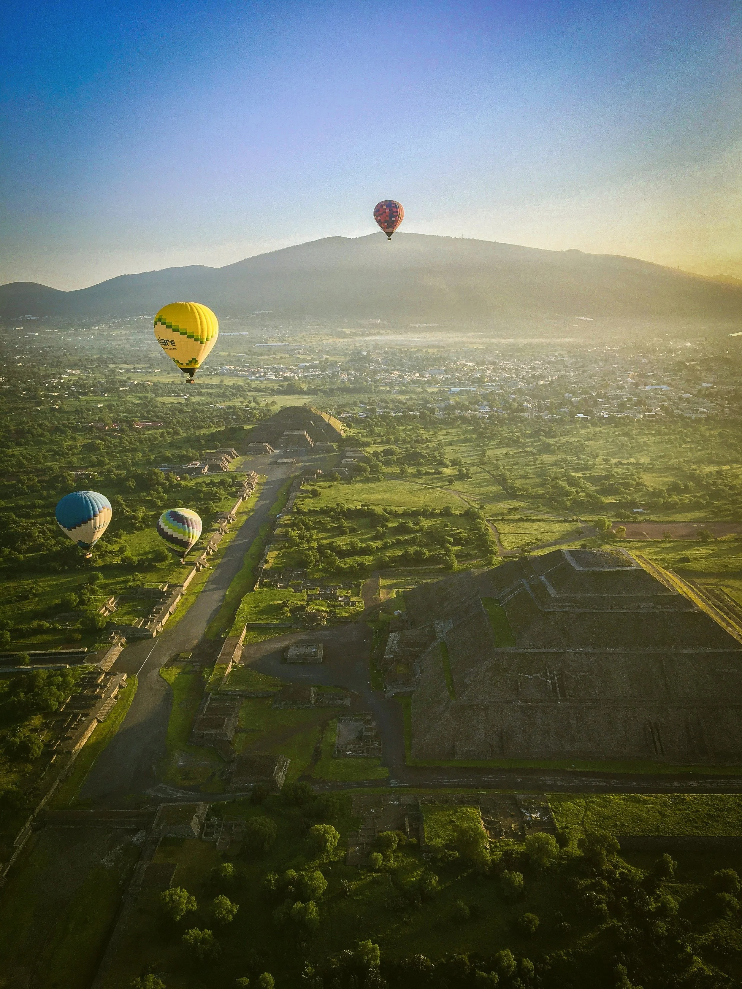 Hot air balloons drifting over a green valley with a pyramid in the foreground, Teotihuacán, Mexico.